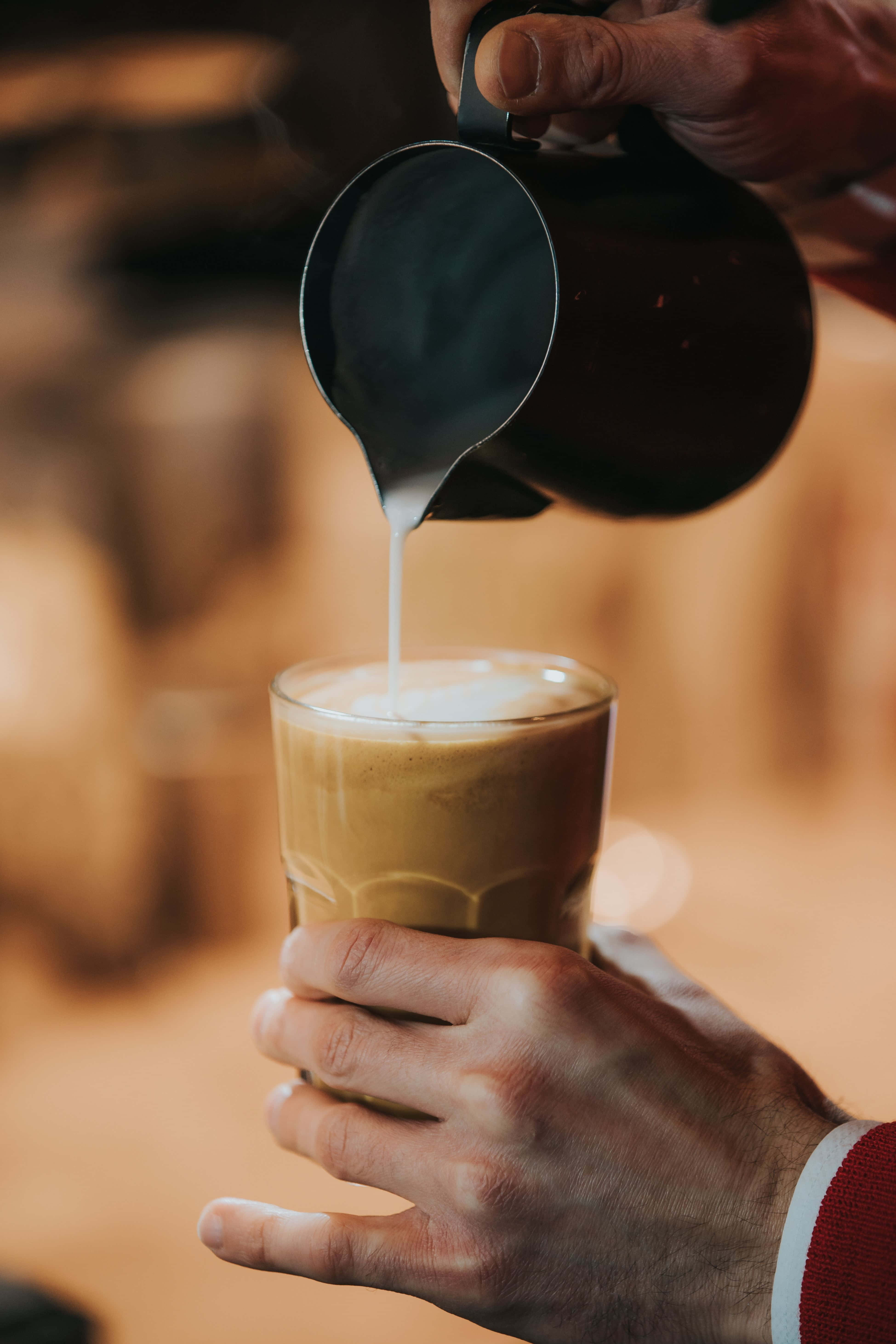 Iced Coffee 桌布 壁紙 — 咖啡師將蒸氣牛奶倒入一杯濃縮咖啡中，在溫暖的金色光線下創造出 creamy 的拉花藝術。