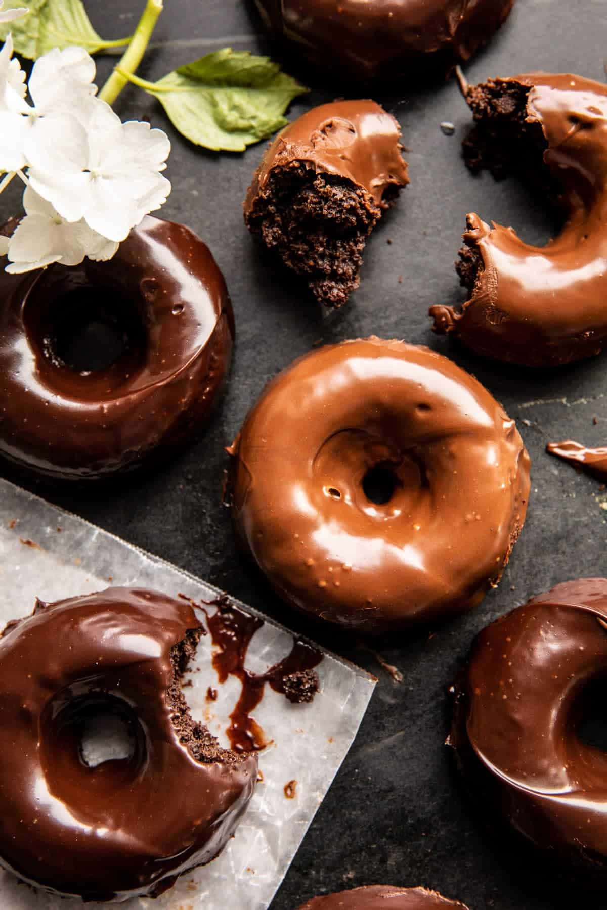 Glazed Donut 桌布 壁紙 — 咬了一口的濃郁巧克力釉面甜甜圈，在深色石板表面上以白色繡球花裝飾。