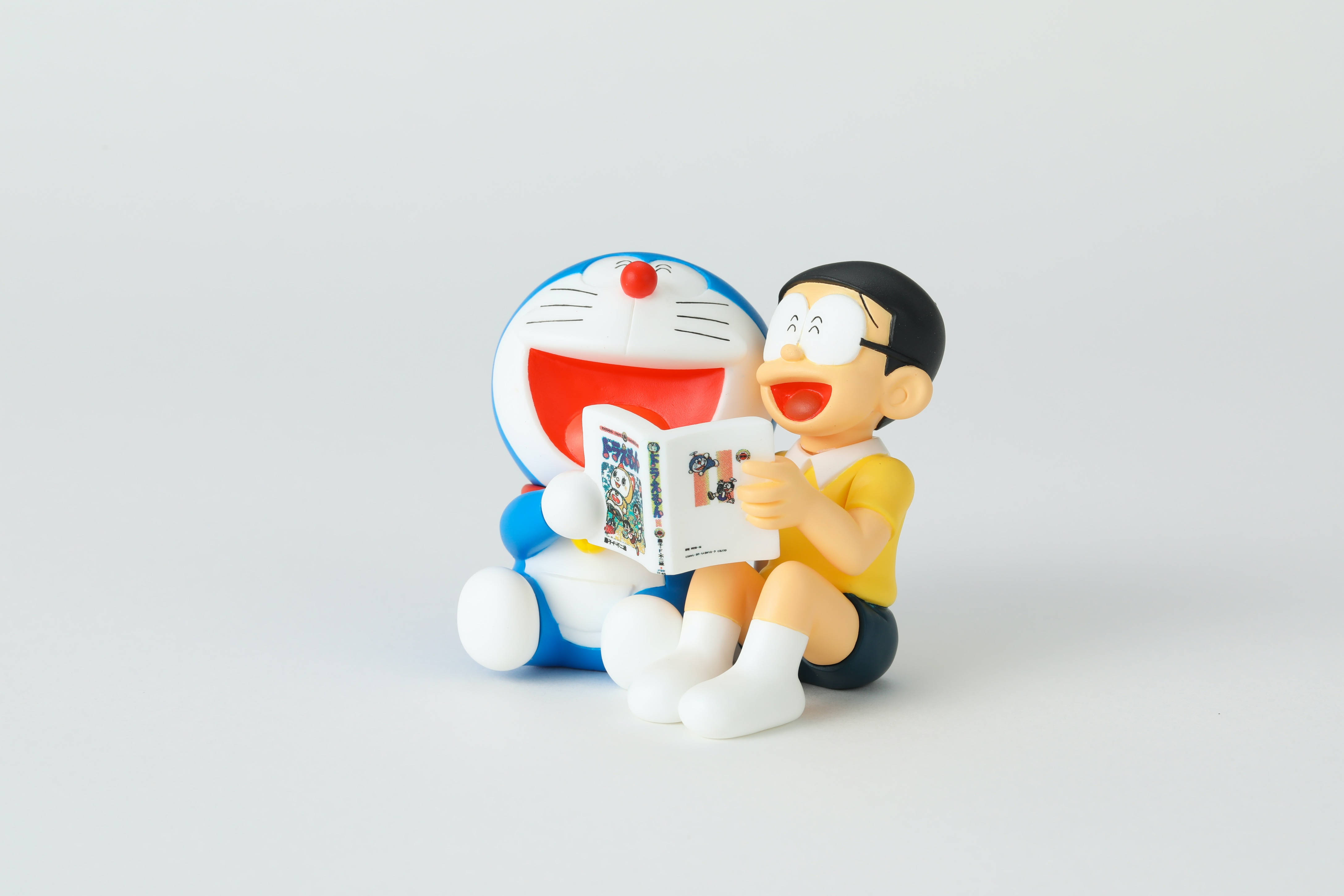 Doraemon 桌布 壁紙 — 哆啦A夢和大雄一起坐著，邊看漫畫邊笑，背景是純白色。