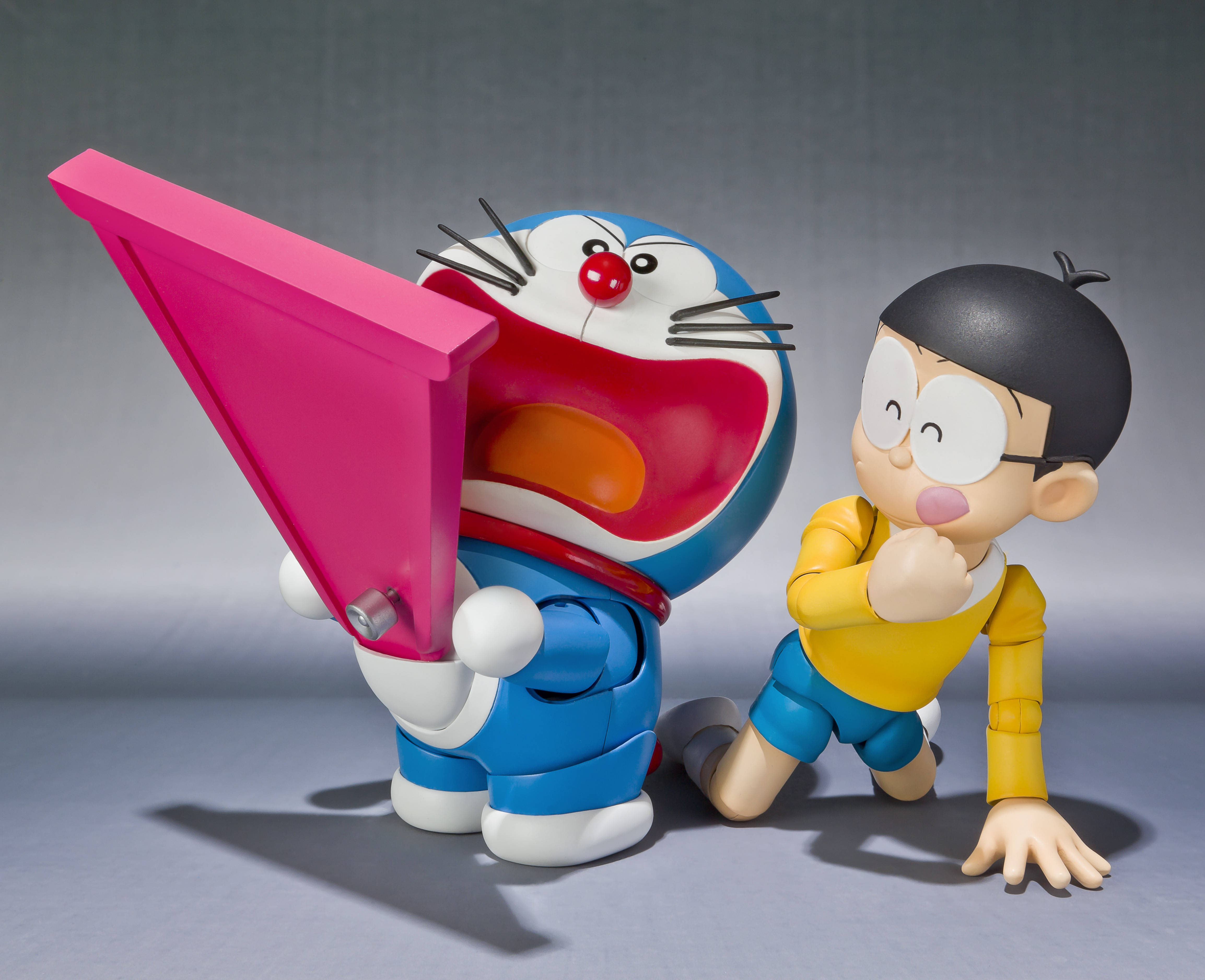 Doraemon 桌布 壁紙 — 哆啦A夢和大雄以俏皮的姿勢擺拍，哆啦A夢在純灰色工作室背景前拿著一個巨大的粉紅色小工具。