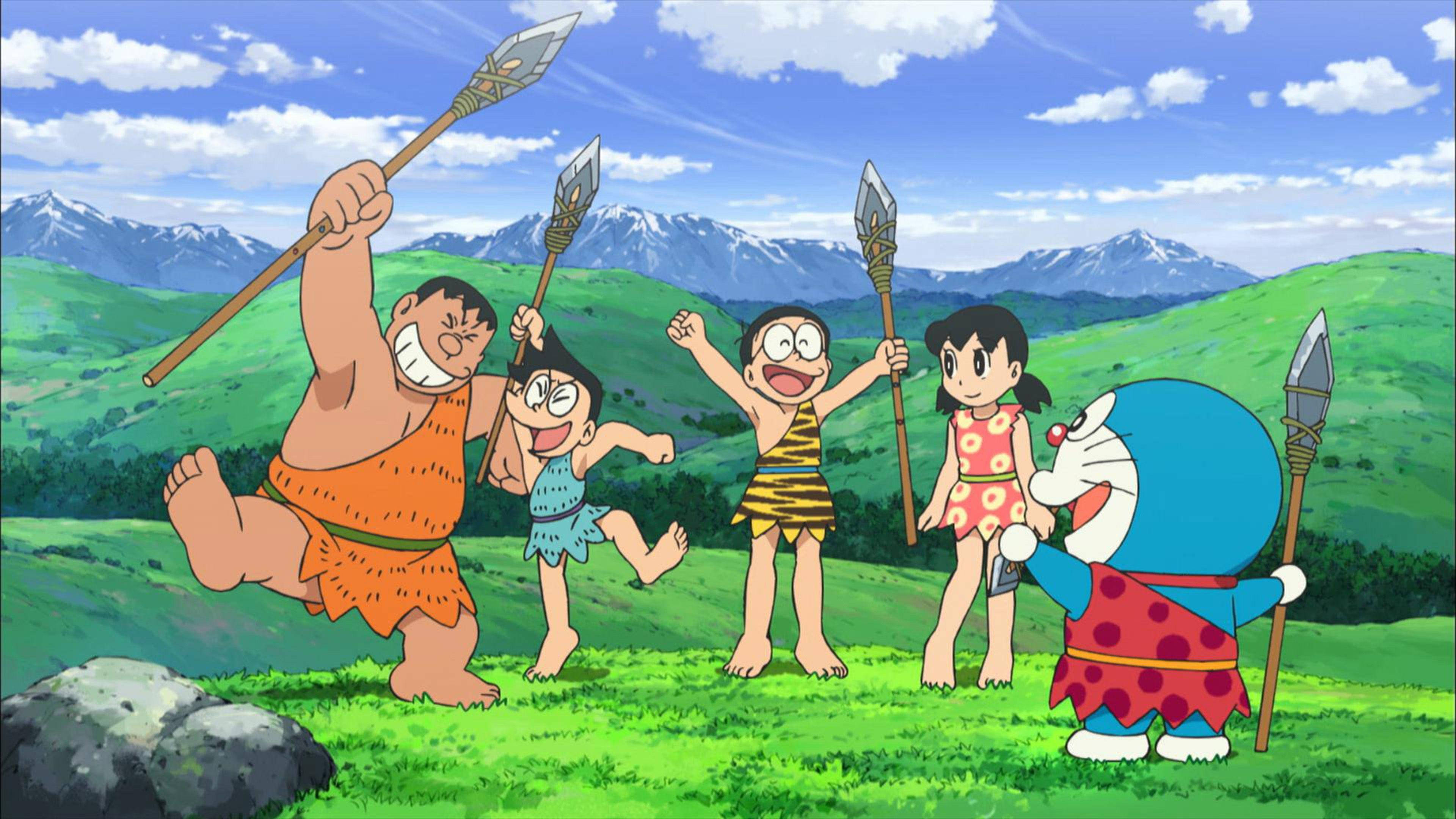 Doraemon And Nobita 桌布 壁紙 — 哆啦A夢和朋友們穿著史前服裝，在藍天下綠草如茵的山坡上，手持長矛，愉快地擺姿勢，遠處有雪山。