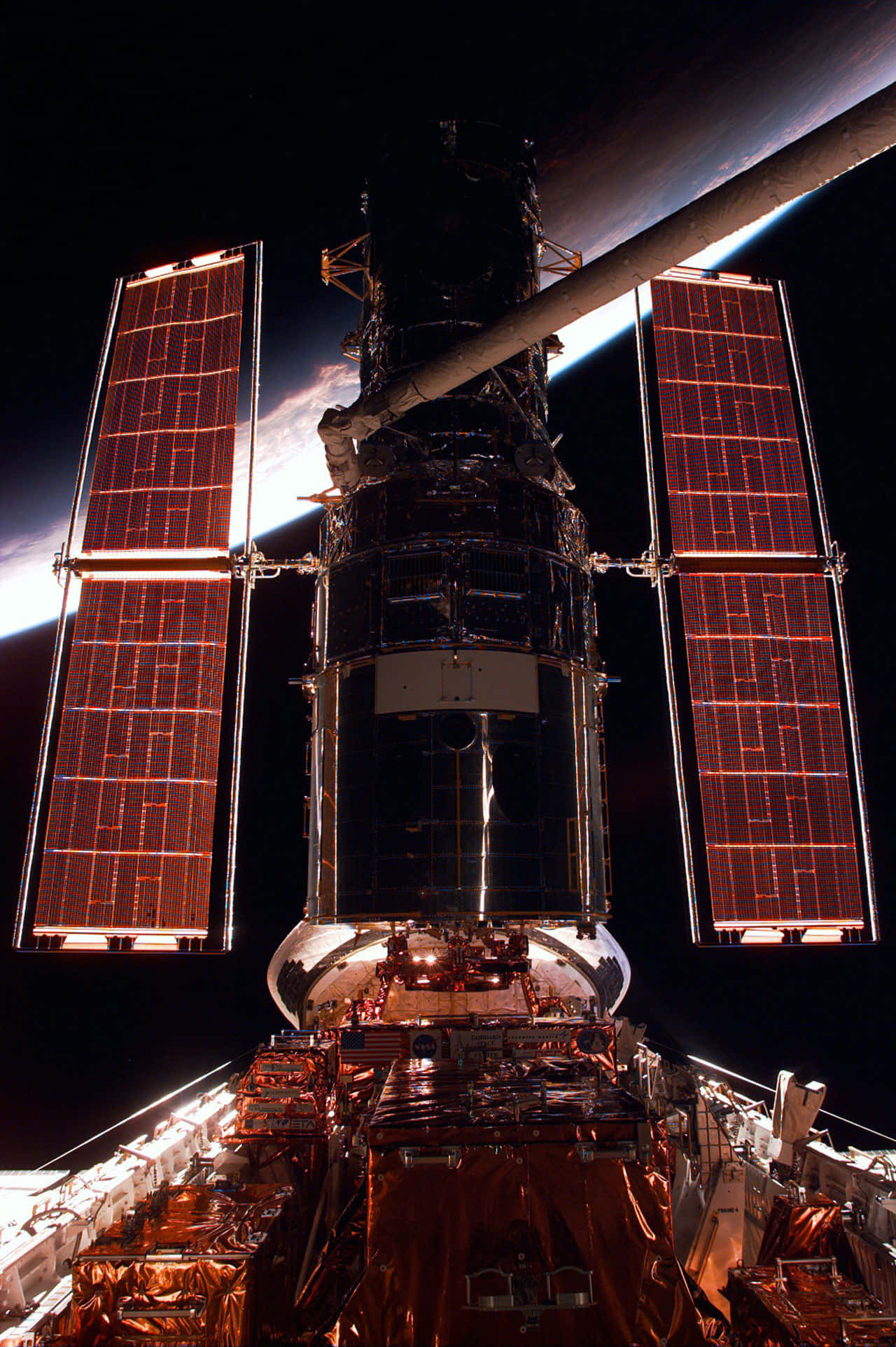 Hubble Space Telescope 桌布 壁紙 — 哈伯太空望遠鏡在漆黑的太空中閃耀著溫暖的橙色太陽能板，背後是地球彎曲的地平線在發光。