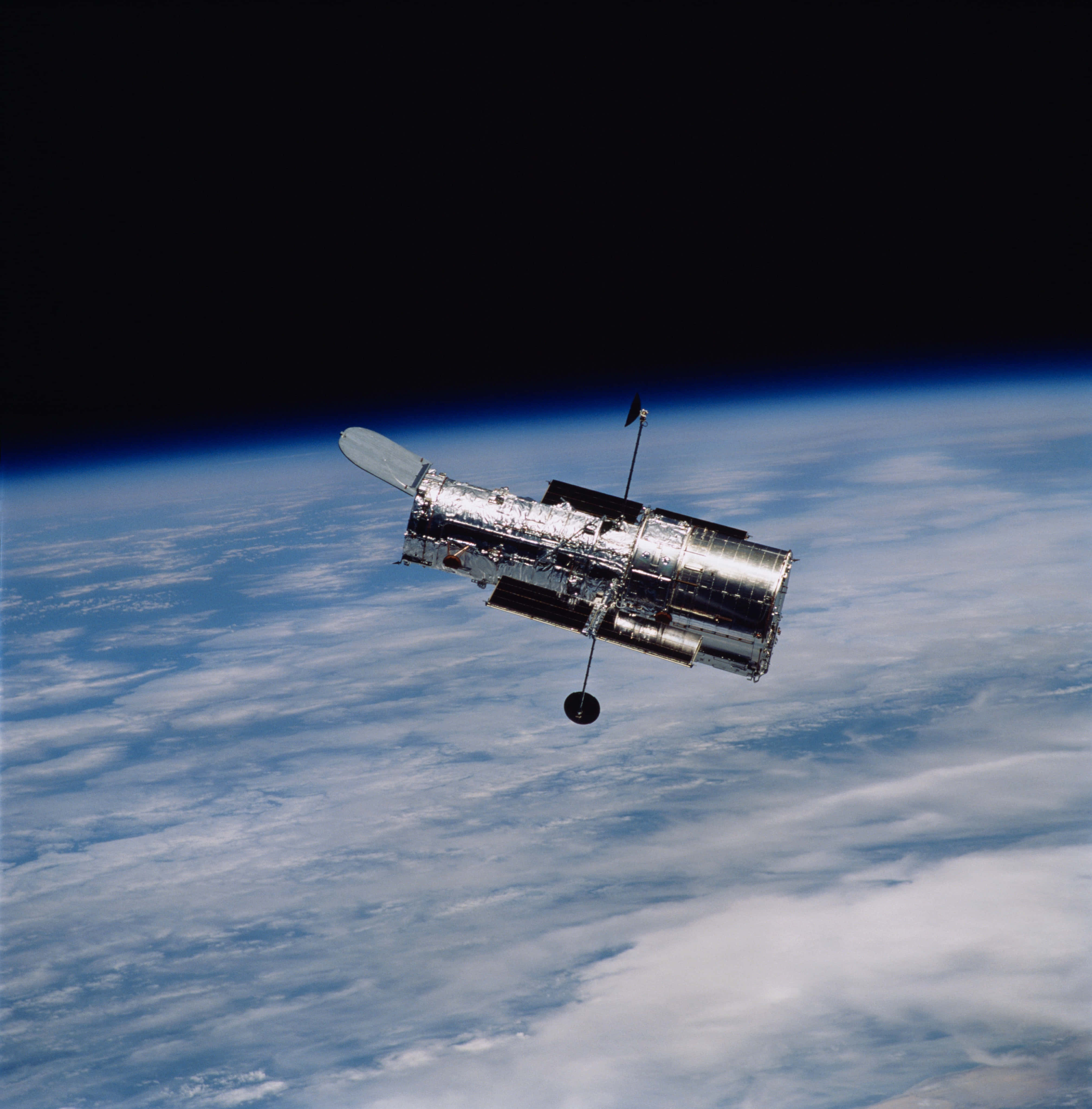 太空 桌布 壁紙 — 哈伯太空望遠鏡在軌道上漂浮，背景是漆黑的太空，下方是地球藍白相間、雲層覆蓋的表面。