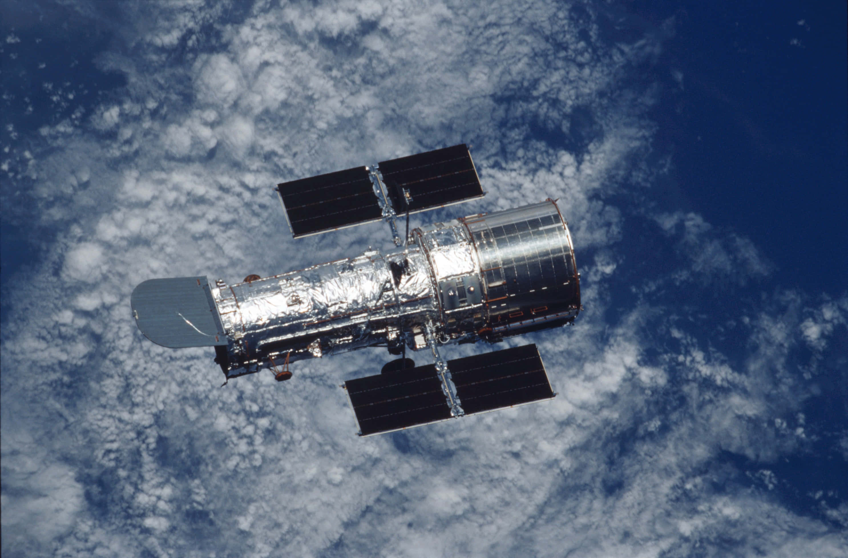 Hubble Space Telescope 桌布 壁紙 — 哈伯太空望遠鏡漂浮在藍白雲層覆蓋的地球表面之上。
