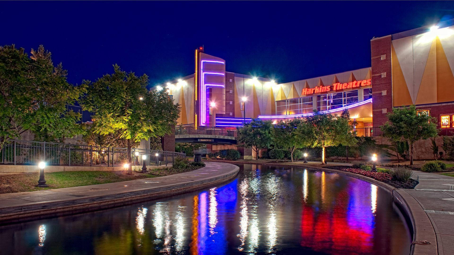 Buildings 桌布 壁紙 — 哈伯斯劇院充滿活力的夜景，被色彩繽紛的霓虹燈照亮，倒映在平靜的水道上，四周環繞著樹木和小徑。