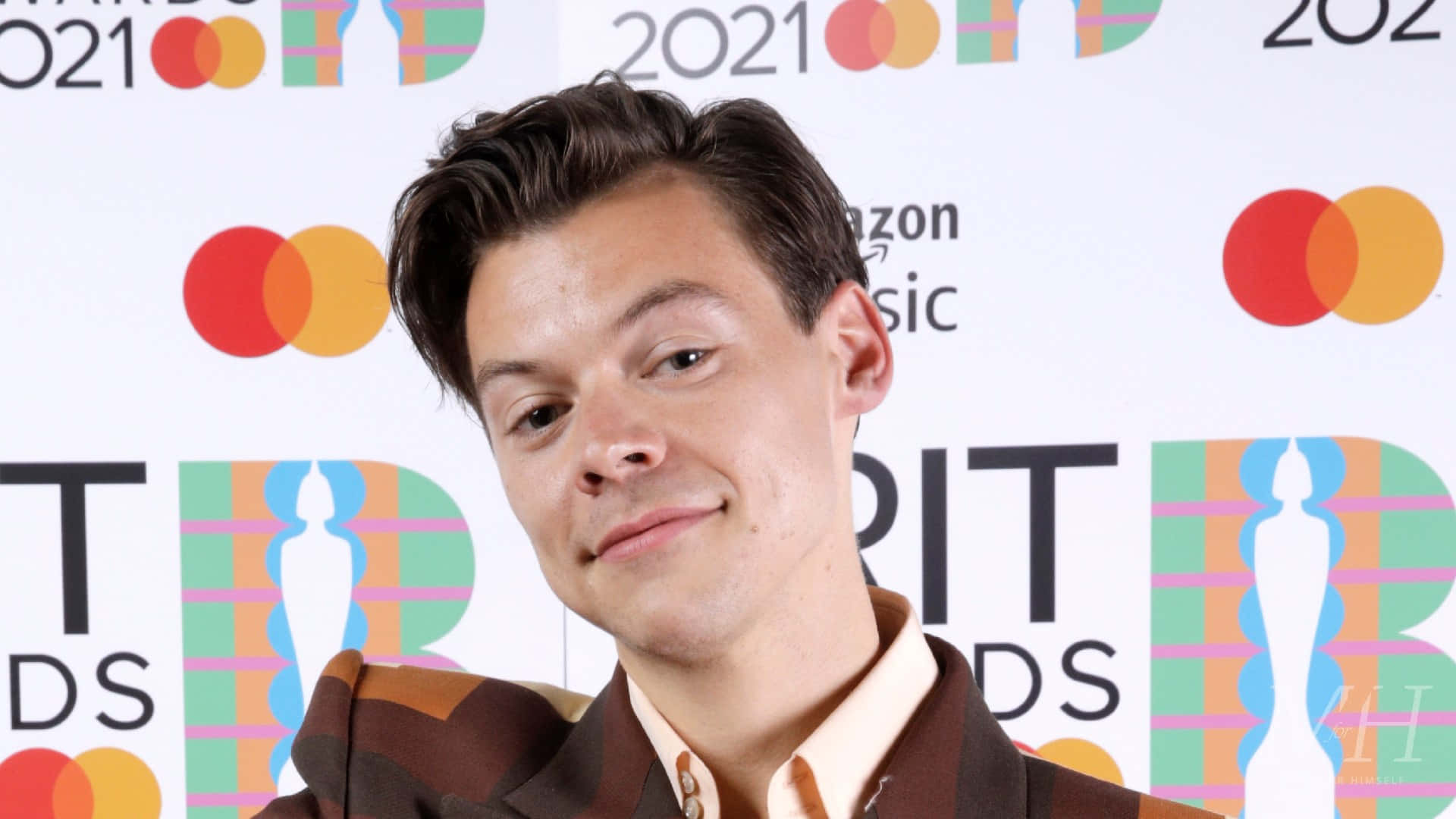 Harry Styles 2021 桌布 壁紙 — 哈利·史泰爾斯在色彩繽紛的 Brit Awards 背景前，帶著 Mastercard 標誌，對著鏡頭微微一笑。