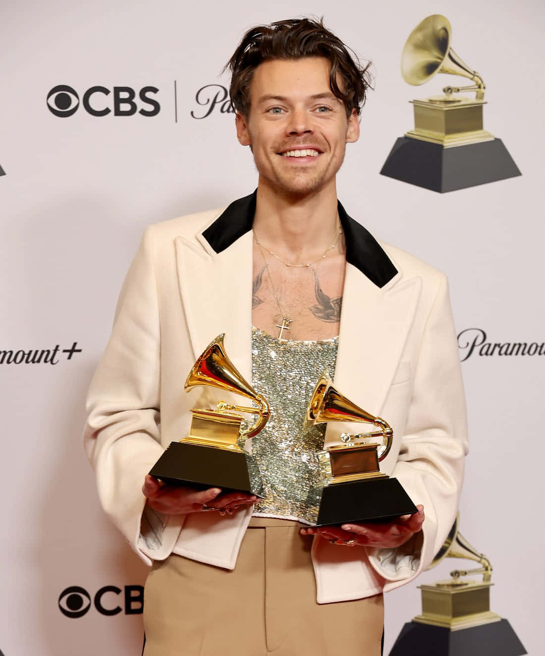 Harry Styles 2021 桌布 壁紙 — 哈利·斯泰爾斯在紅地毯活動中手持兩座葛萊美獎盃，身後有CBS和派拉蒙標誌，笑容滿面。