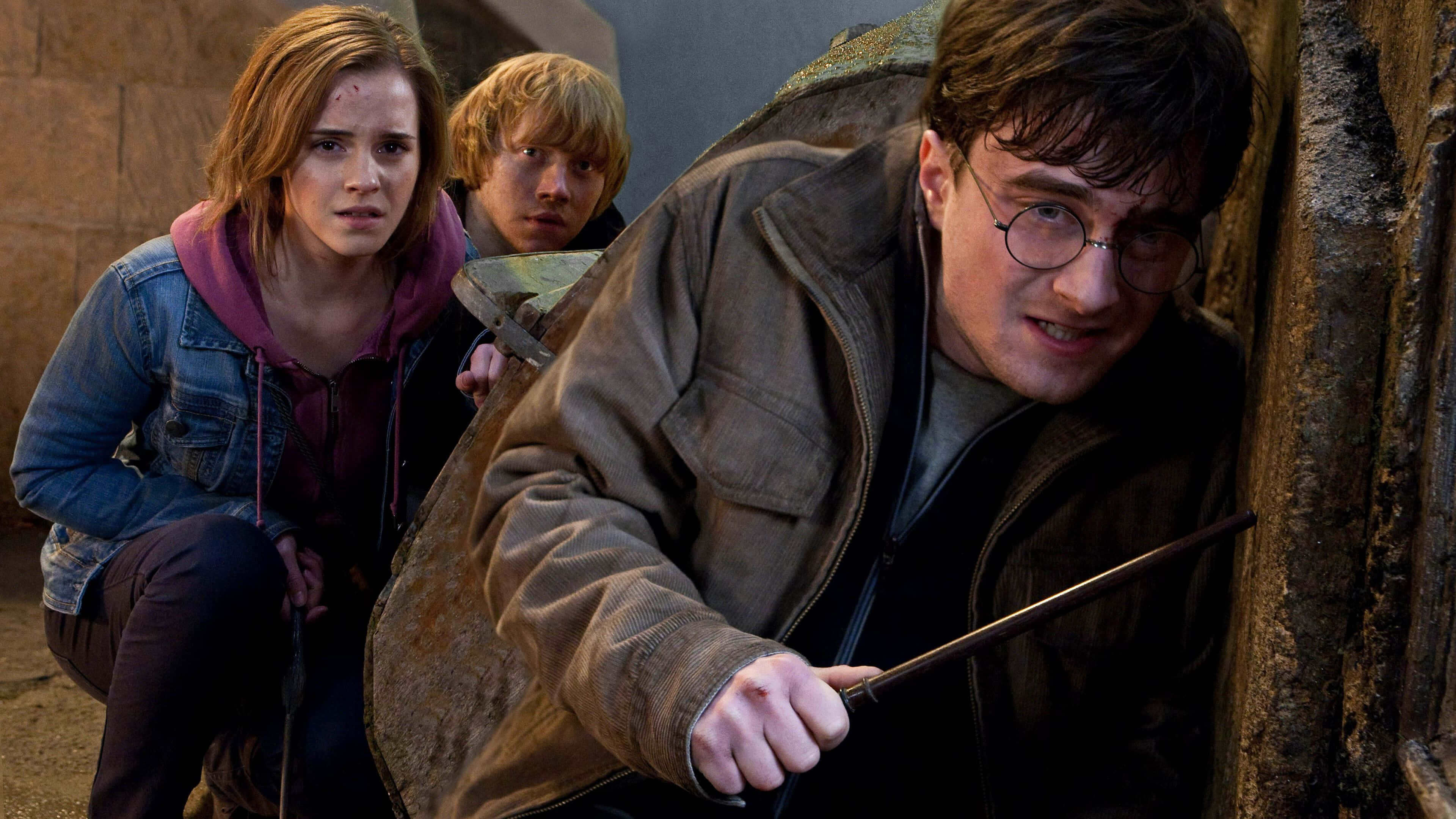 Harry Potter 4K 桌布 壁紙 — 哈利波特小心翼翼地從石牆後探頭張望，旁邊的妙麗和榮恩緊張地握著魔杖。