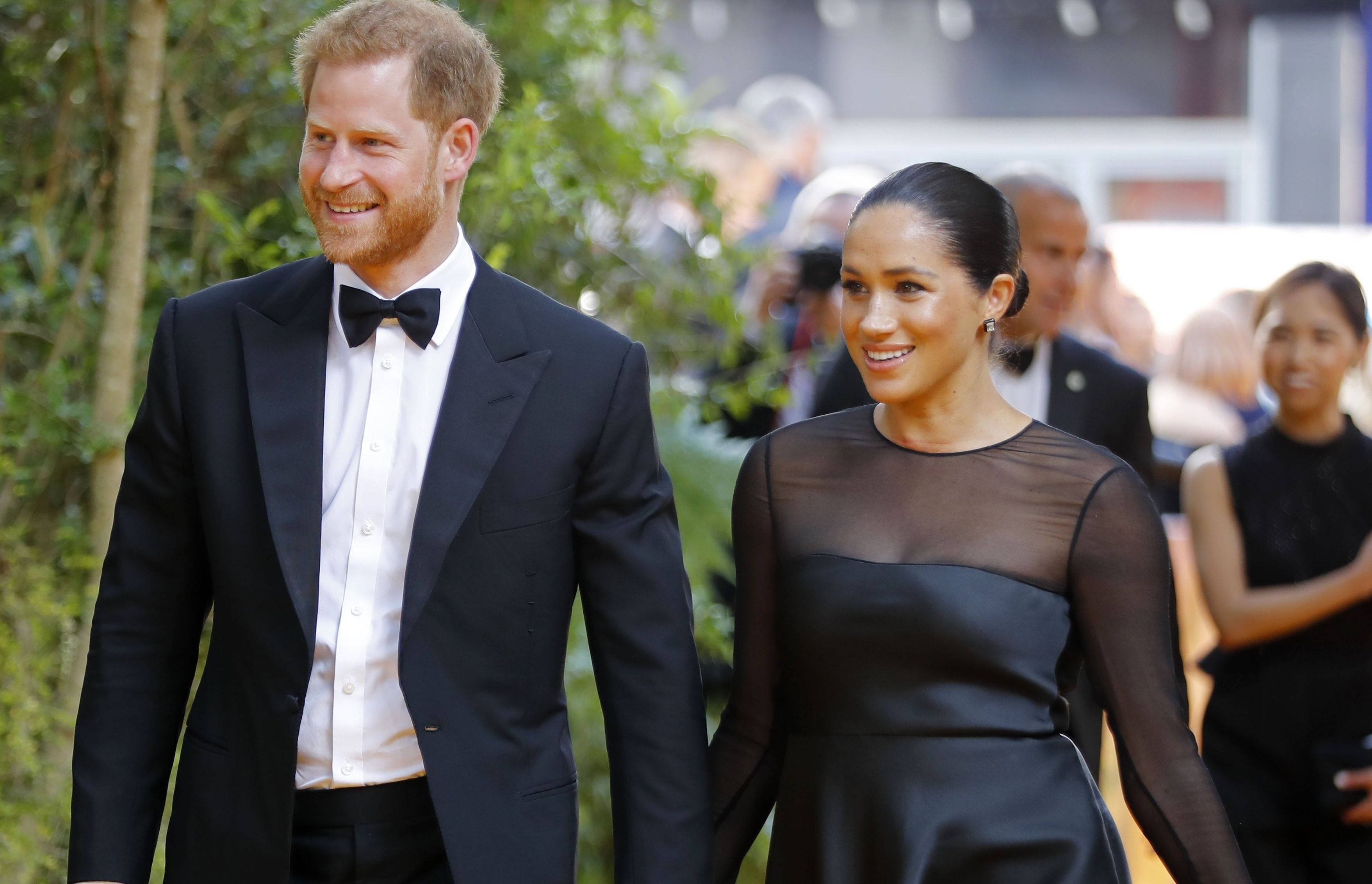 Meghan Markle 桌布 壁紙 — 哈利王子和梅根·馬克爾手牽手穿著正式黑色服裝，在戶外活動中微笑。