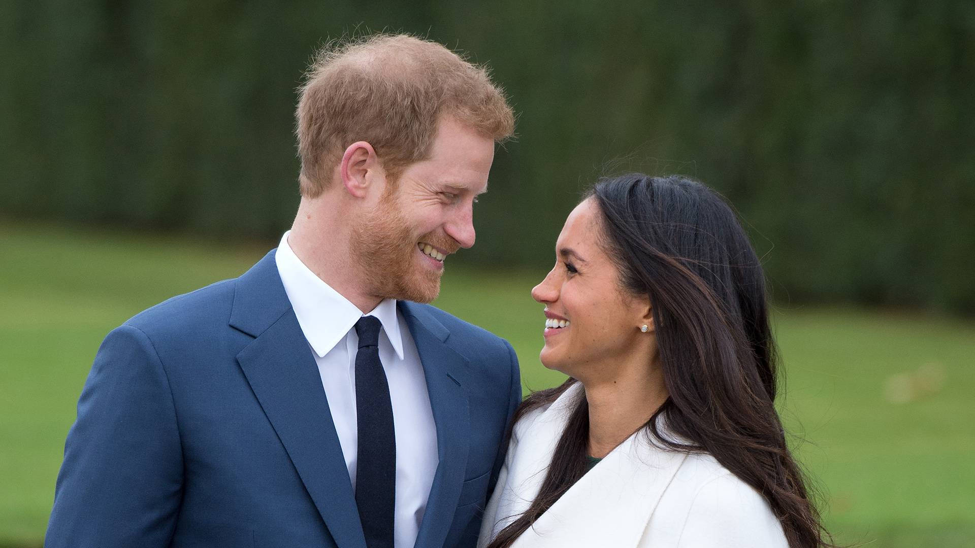 Meghan Markle 桌布 壁紙 — 哈利王子與梅根馬克爾在草地上親密地站在一起，分享溫暖的笑容。