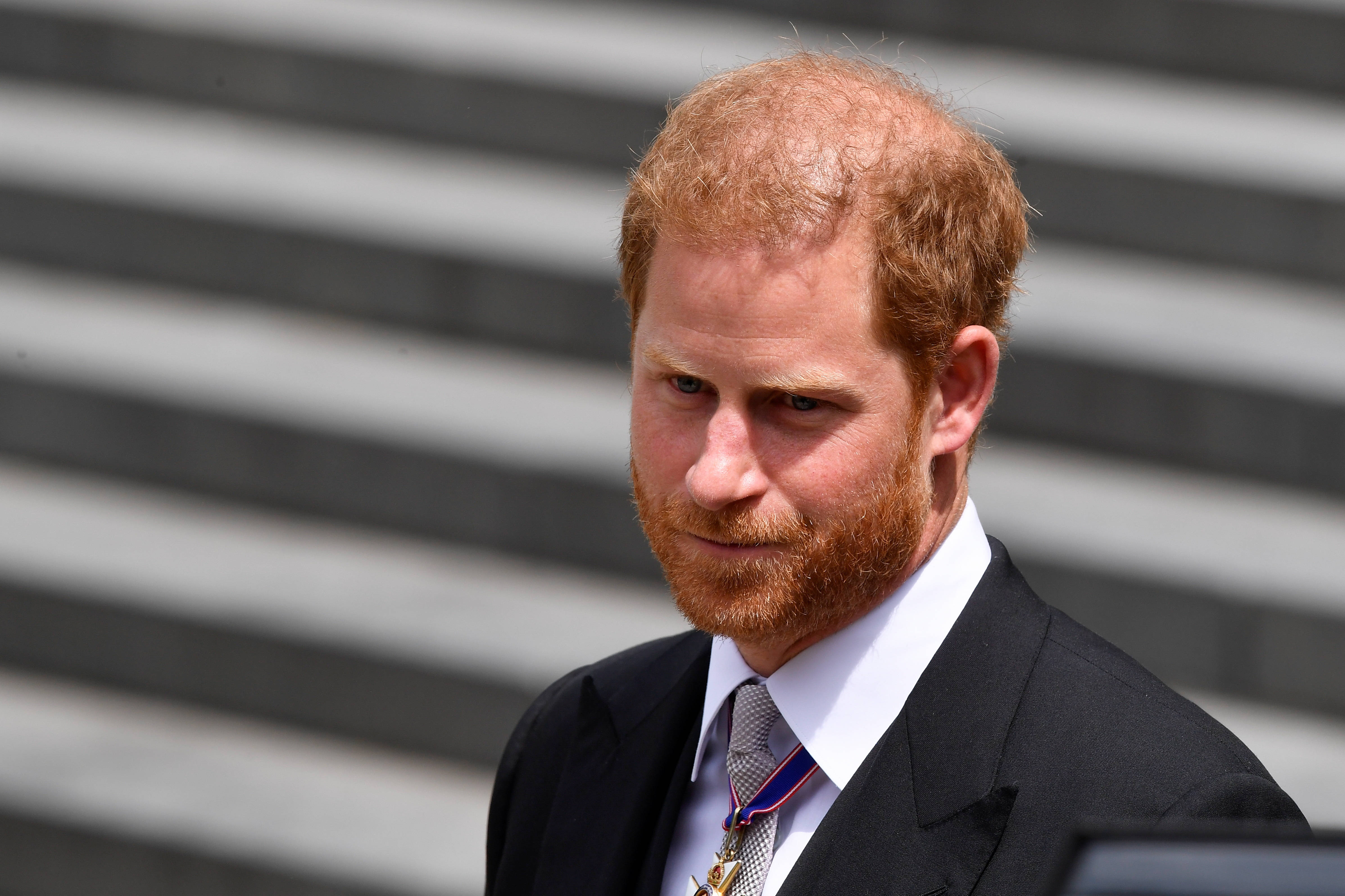 Prince 桌布 壁紙 — 哈利王子身穿深色西裝和勳章，在明亮的日光下，以模糊的灰色台階為背景莊嚴地站立。