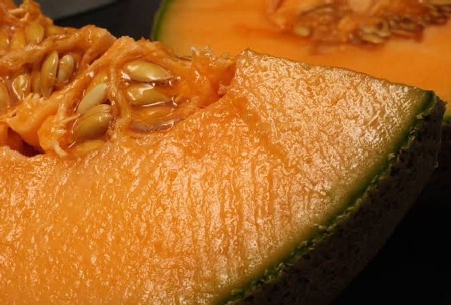 Fruit 桌布 壁紙 — 哈密瓜多汁切片的特寫，露出橙色果肉、種子和綠色外皮，背景深色。