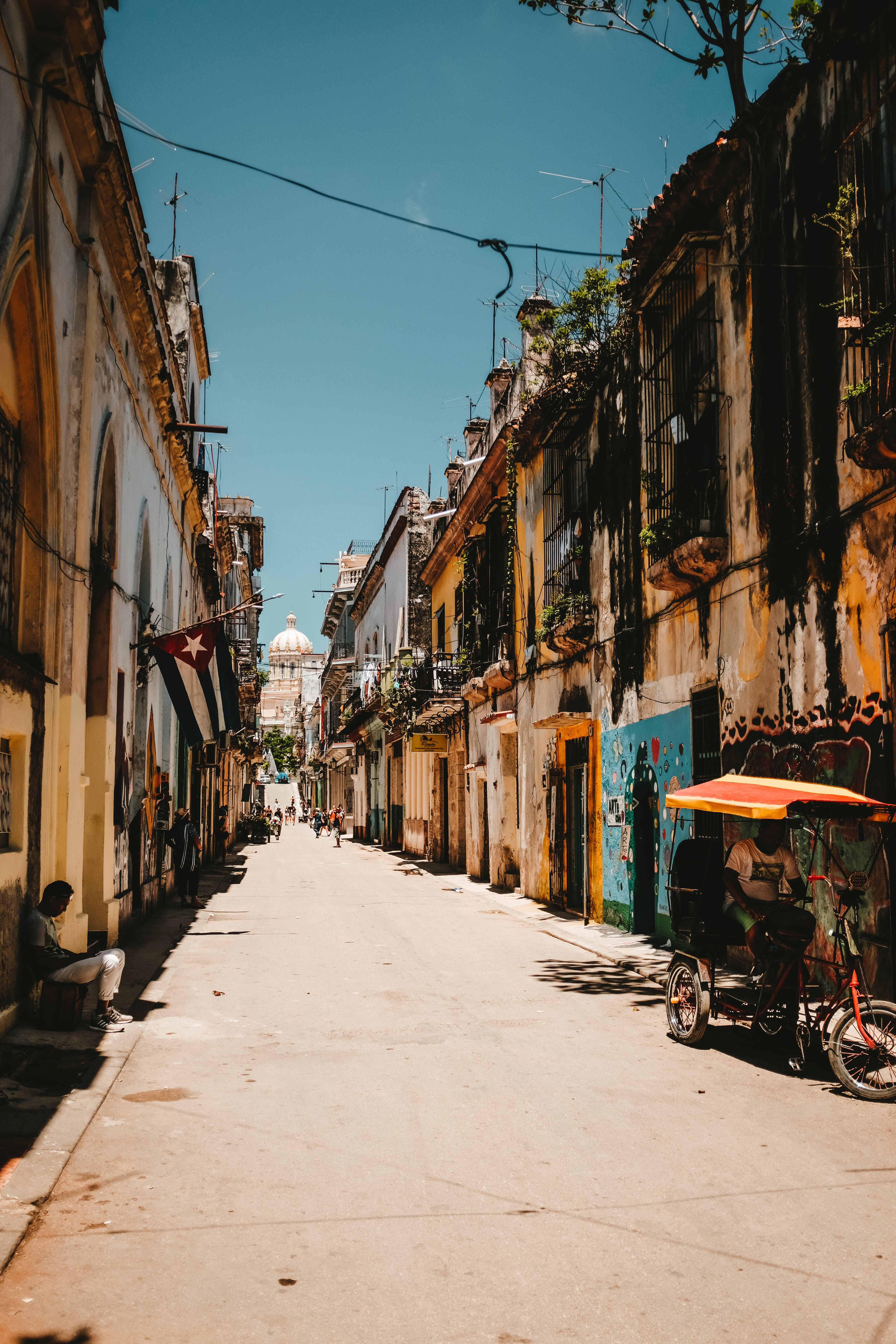 Cuba 桌布 壁紙 — 哈瓦那一條陽光普照的狹窄街道，兩旁是風化的殖民時期建築，在清澈的藍天下有鮮豔的塗鴉。