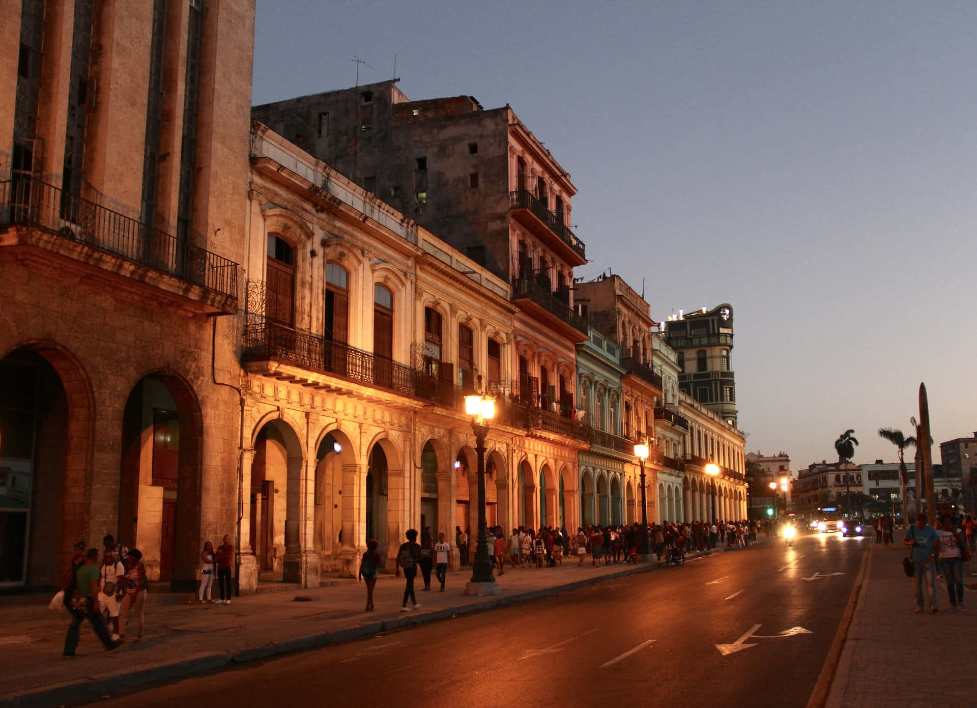 Cuba 桌布 壁紙 — 哈瓦那充滿活力的黃昏街道，歷史悠久的殖民建築在溫暖的路燈下閃耀，行人沿著人行道漫步。