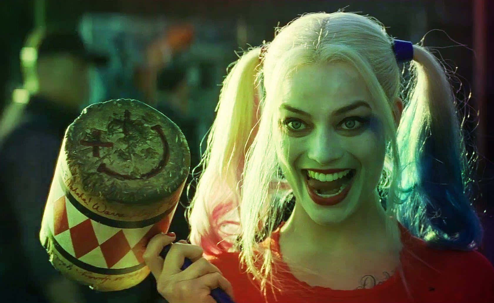 The Suicide Squad 桌布 壁紙 — 哈莉·奎茵在模糊的城市背景下，狂野地咧嘴笑著，手持她那帶有塗鴉笑臉的標誌性大錘。