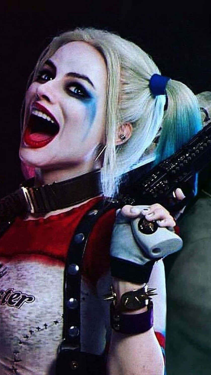 Margot Robbie Harley Quinn 桌布 壁紙 — 哈莉·奎茵在黑暗環境中狂野地咧嘴笑，手持步槍，擁有標誌性的金色雙馬尾和紅唇。