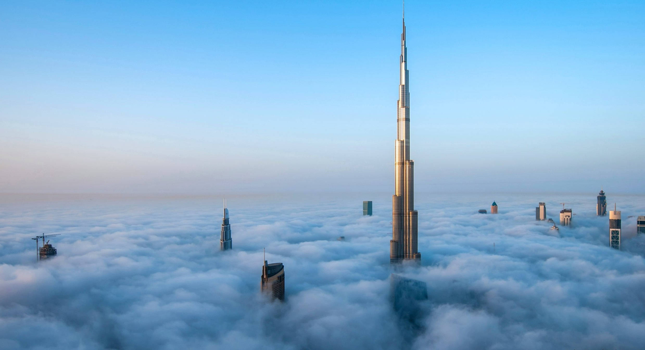 Arab 桌布 壁紙 — 哈里發塔刺穿雲海，其他摩天大樓在晴朗的藍天下從薄霧中浮現。