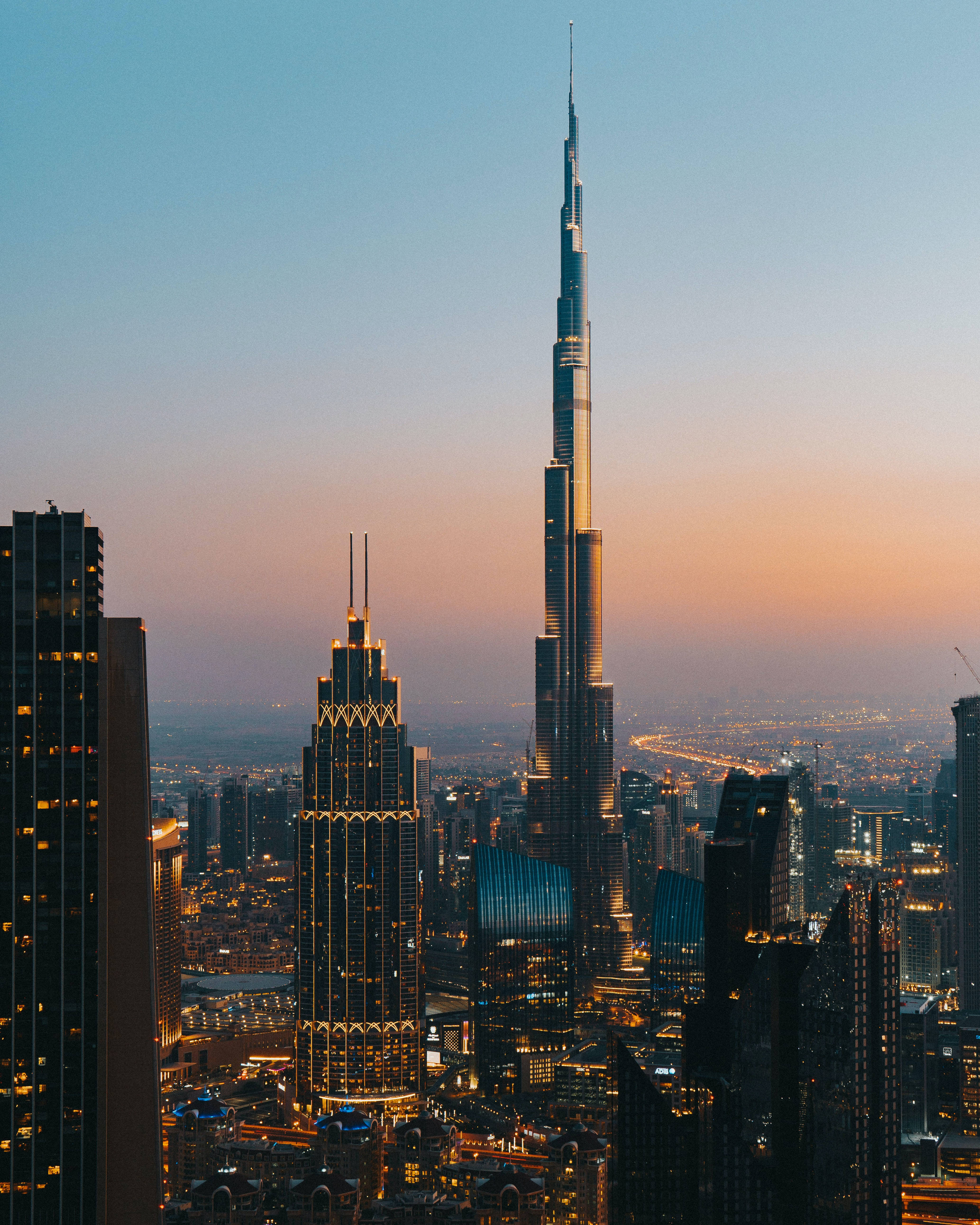 Skyscraper 桌布 壁紙 — 哈里發塔在日落時分聳立於杜拜天際線之上，金色燈光在漸變的天空中閃耀。