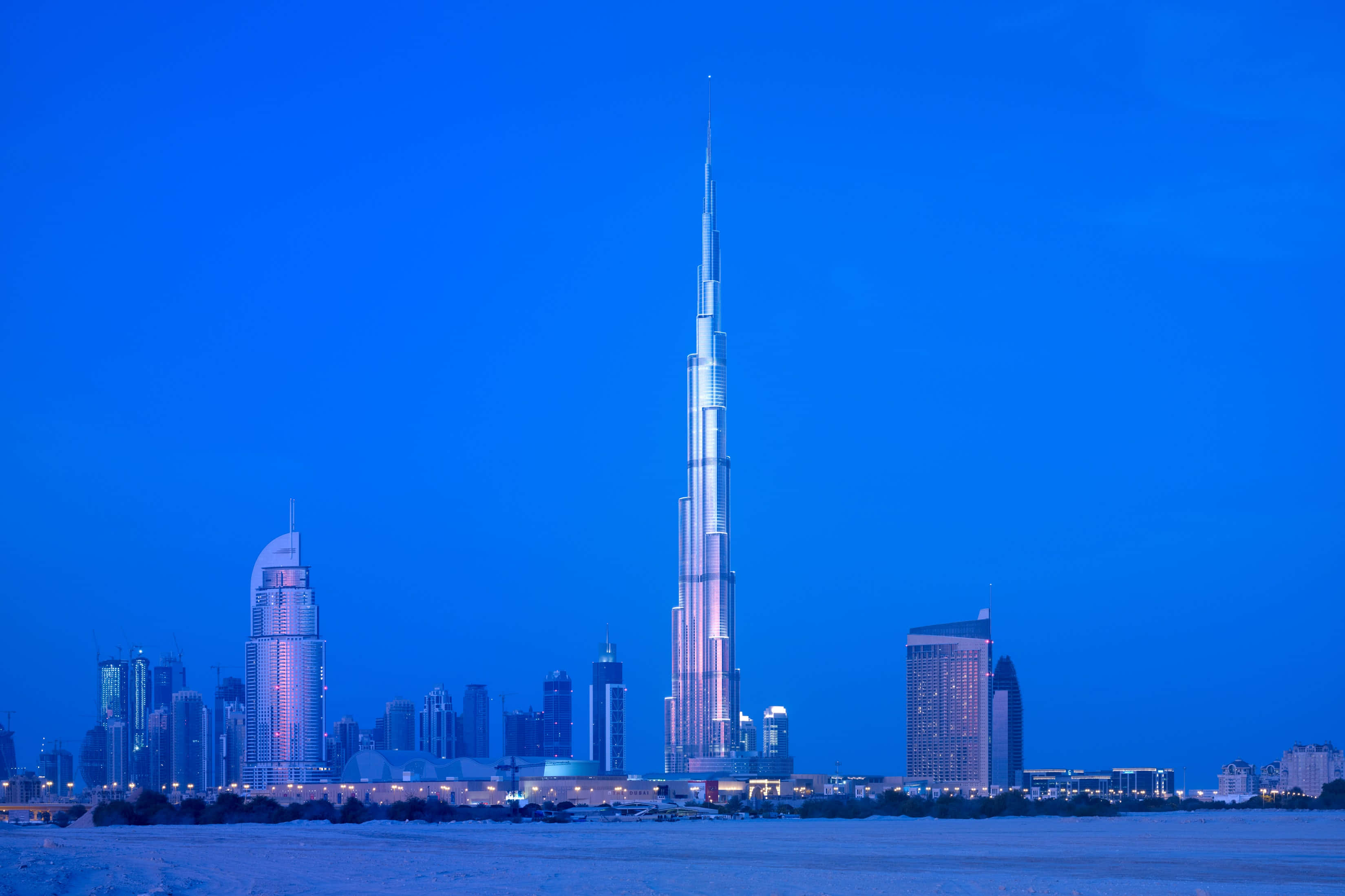 Burj Khalifa 桌布 壁紙 — 哈里發塔在暮色中聳立於杜拜天際線之上，深藍色的天空和閃爍的城市燈光倒映在水面上。