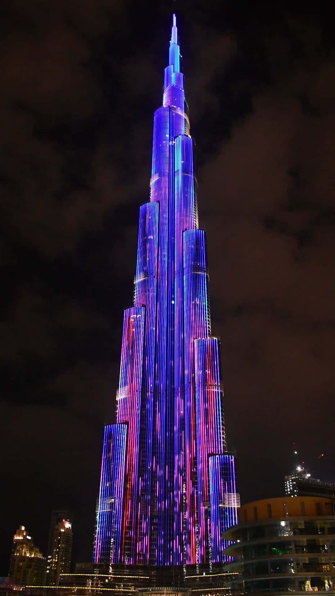 Building 桌布 壁紙 — 哈里發塔在黑暗多雲的夜空下，以電光藍和洋紅色璀璨亮起。