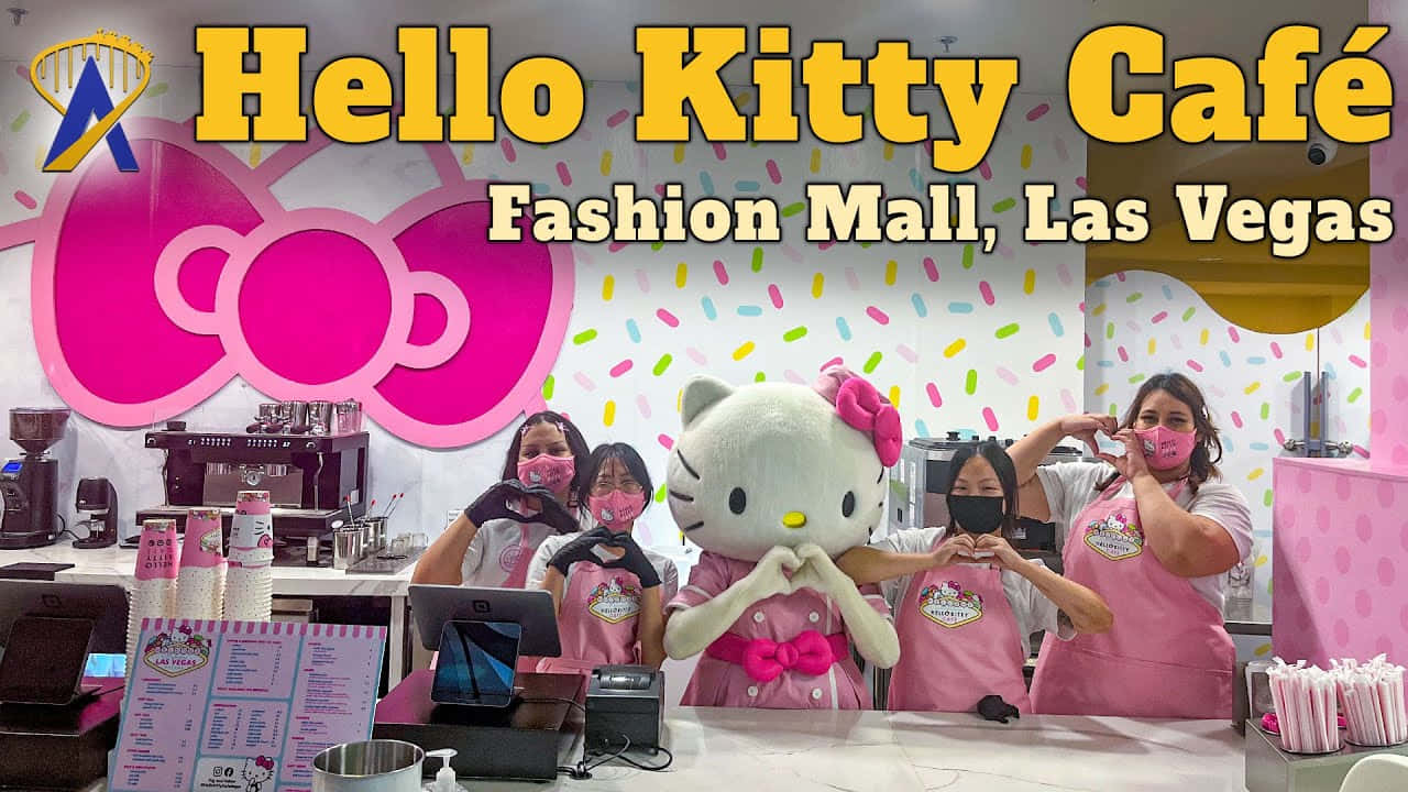 Hello Kitty 桌布 壁紙 — 員工和一個巨大的Hello Kitty吉祥物在明亮的招牌下，於粉紅色咖啡櫃檯後面擺出心形手勢。