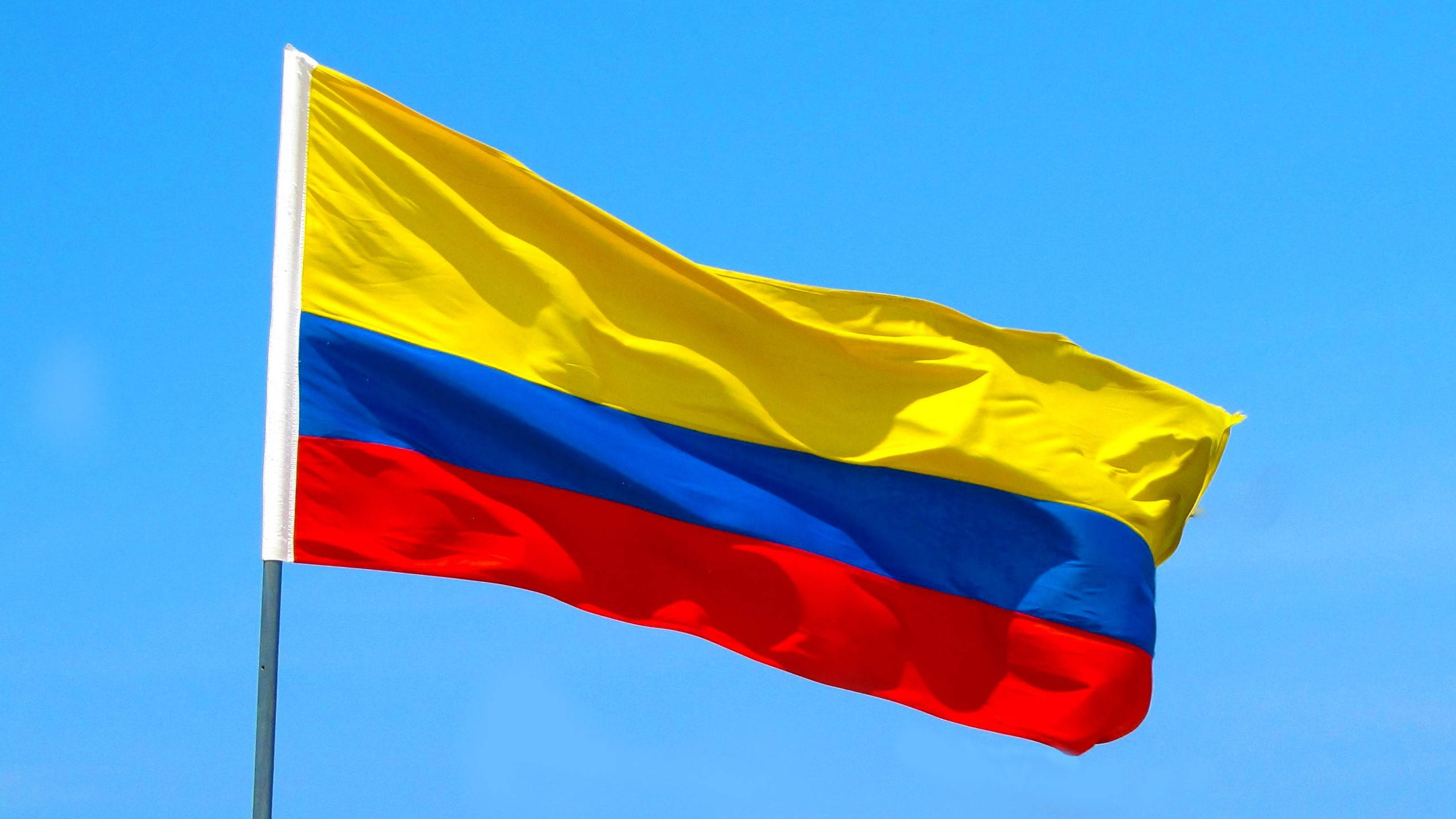 Colombia Flag 桌布 壁紙 — 哥倫比亞國旗上的黃、藍、紅條紋在清澈的藍天下動態飄揚。