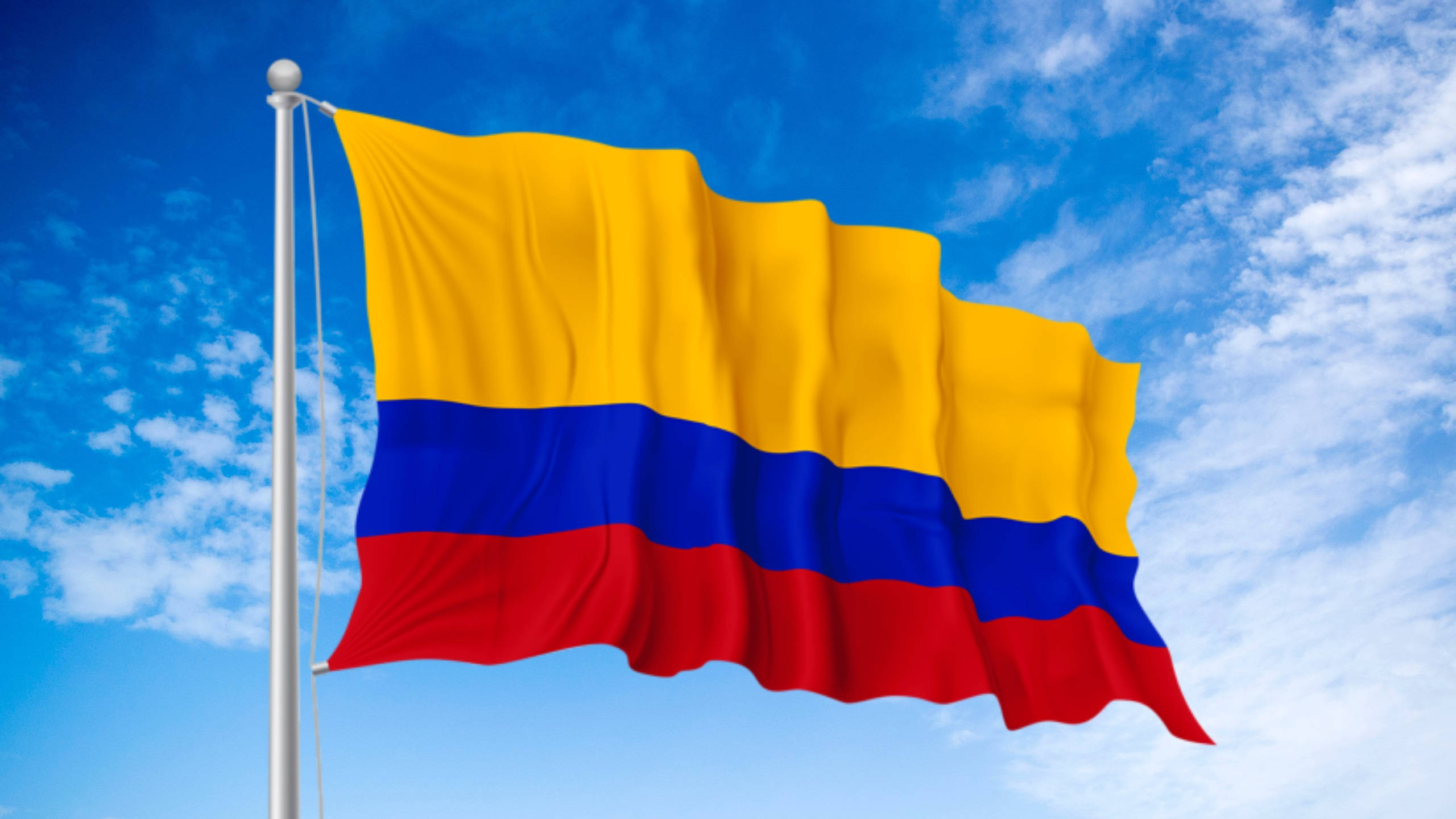 Colombia Flag 桌布 壁紙 — 哥倫比亞國旗在明亮的藍天和散落的白色雲朵中自豪地飄揚。