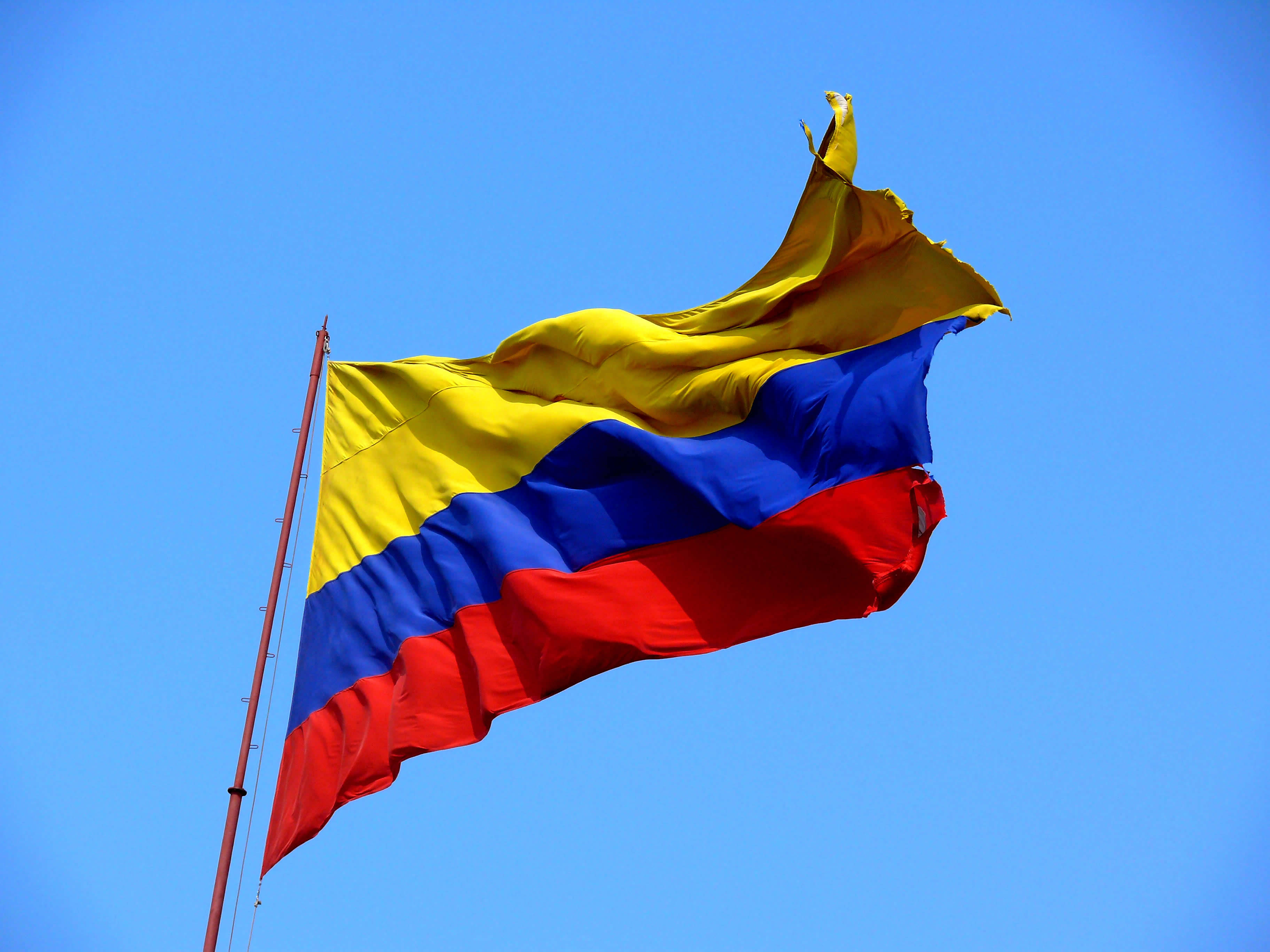 Colombia Flag 桌布 壁紙 — 哥倫比亞國旗在清澈的藍天下動態飄揚，帶有鮮明的黃、藍、紅條紋。