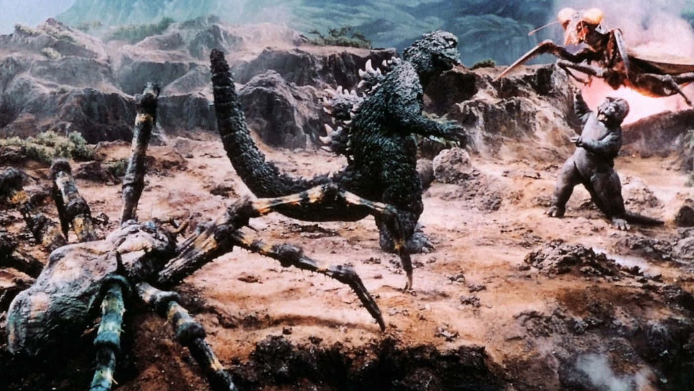 Classic Godzilla 桌布 壁紙 — 哥吉拉在崎嶇的山地地形中與巨型蜘蛛和蛾狀怪獸戰鬥，煙霧和碎片四散。