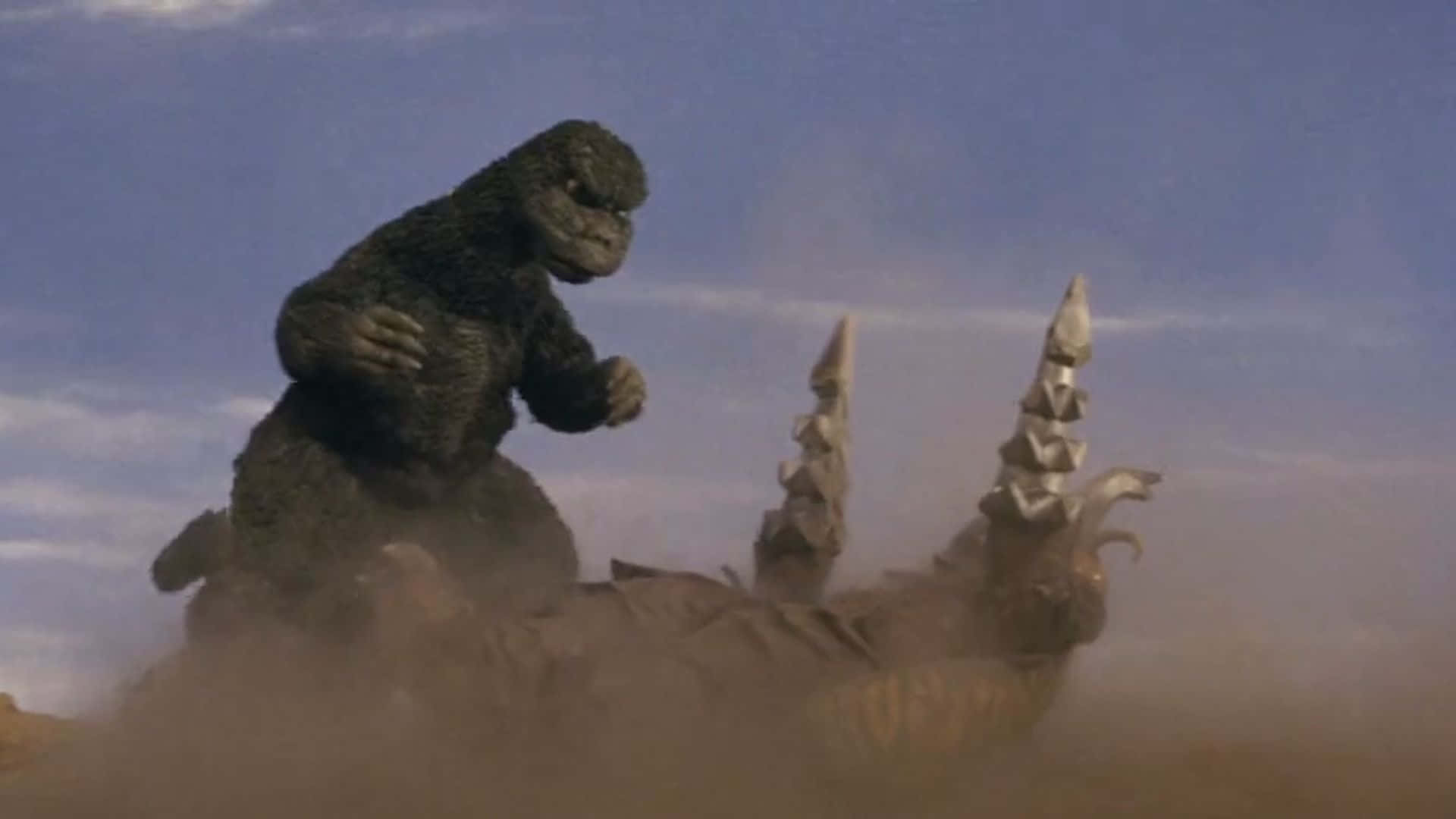 Godzilla Vs Megalon 桌布 壁紙 — 哥吉拉在晴朗藍天下，塵土飛揚的沙漠戰場上，勝利地站在被擊敗的怪物之上。