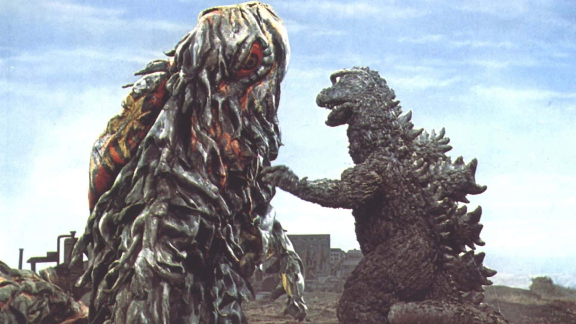 Godzilla Vs Hedorah 桌布 壁紙 — 哥吉拉在淡藍色天空下，於廢墟城市景觀中面對一個怪誕、融化的怪物。