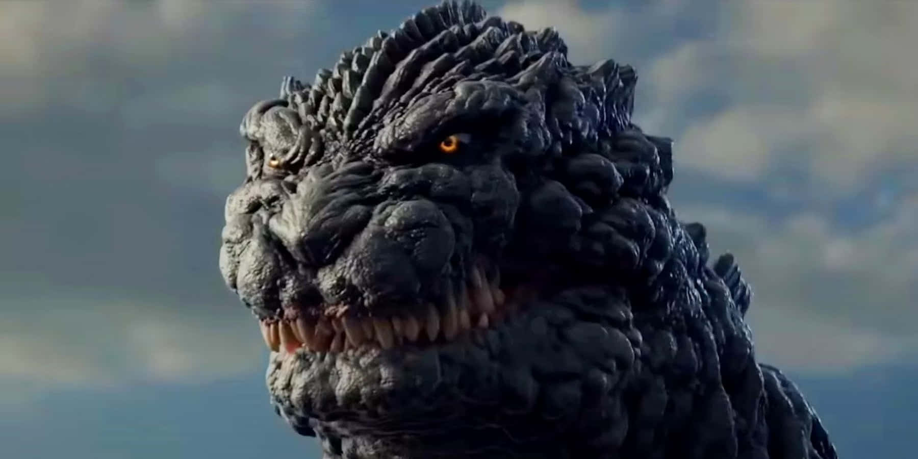 monsters 桌布 壁紙 — 哥吉拉巨大鱗片頭部的特寫，發光的橙色眼睛和鋒利的牙齒，背景是多雲的天空。
