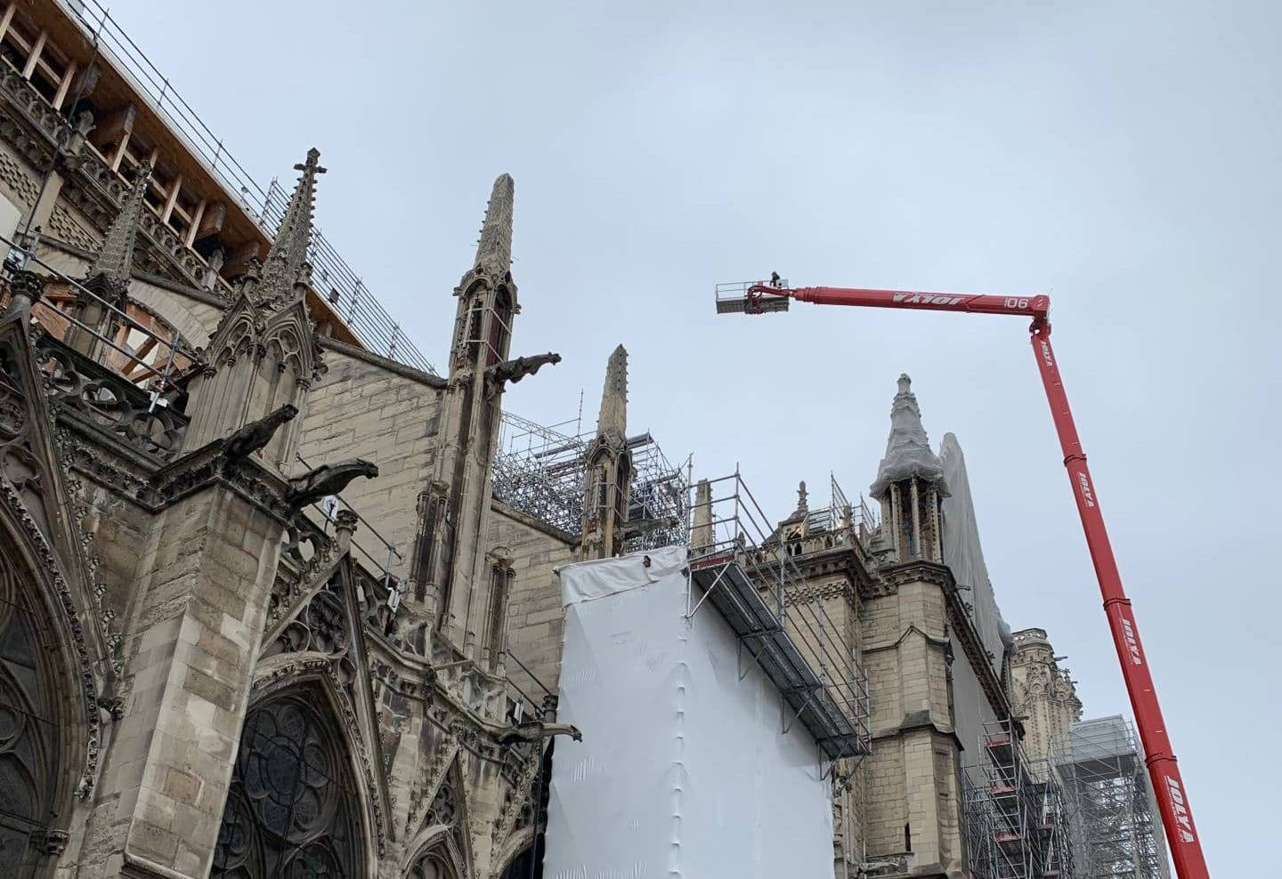 Notre Dame 桌布 壁紙 — 哥德式大教堂正在修復中，紅色起重機和鷹架襯著多雲的天空。