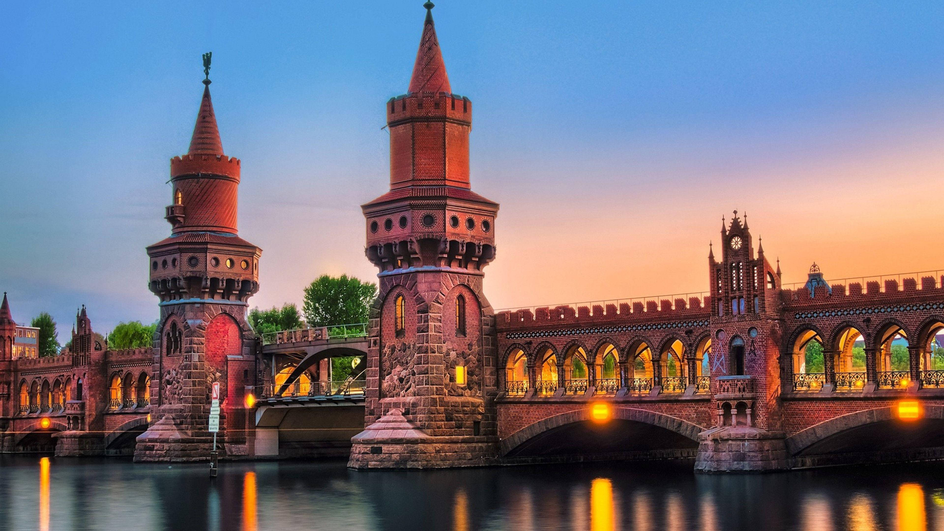 Berlin 桌布 壁紙 — 哥德式磚橋，帶有塔樓和拱形步道，在日落時分溫暖地照耀在平靜的水面上。