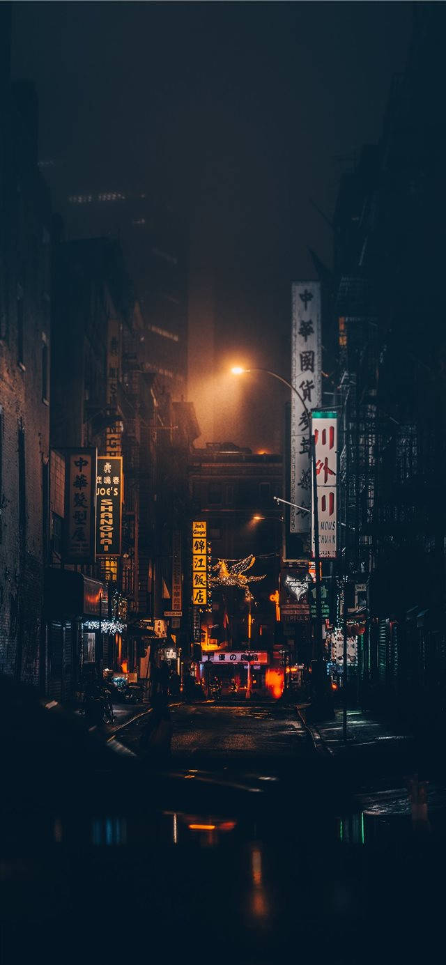 iPhone 桌布 壁紙 — 唐人街一條狹窄的雨夜街道，沐浴在溫暖的霓虹燈光中，倒映在濕漉漉的路面上。