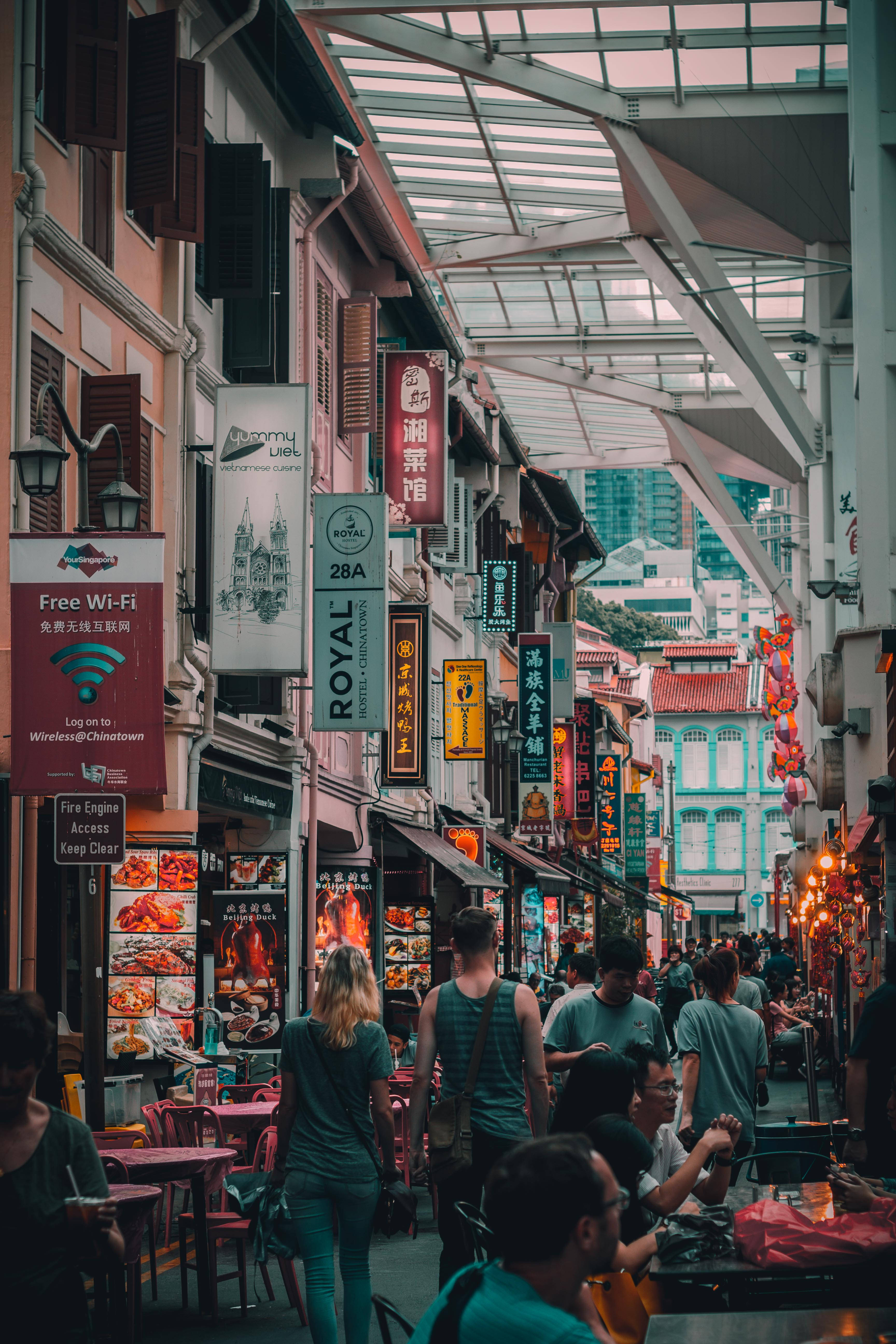 Singapore 桌布 壁紙 — 唐人街一條繁忙的有蓋小巷，充滿行人、充滿活力的美食攤位和玻璃屋頂下色彩繽紛的懸掛招牌。