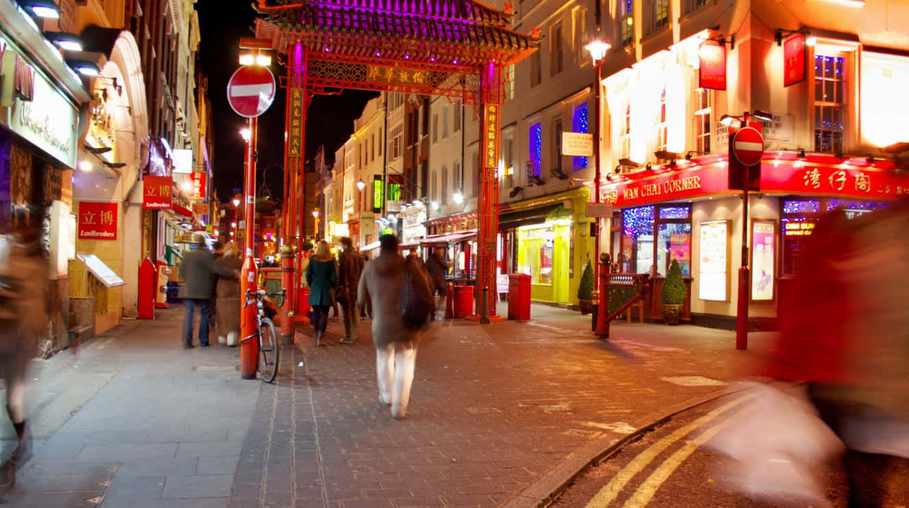 Red Light District 桌布 壁紙 — 唐人街一條繁華的夜晚街道，被鮮紅的燈籠和發光的商店招牌照亮，模糊的行人走過。