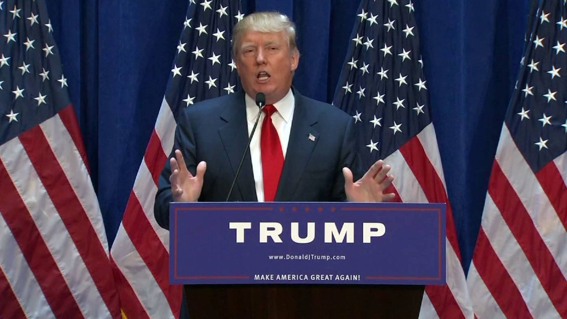 川普 桌布 壁紙 — 唐納·川普在講台上熱情演講，'TRUMP'和'MAKE AMERICA GREAT AGAIN'文字兩旁有美國國旗。