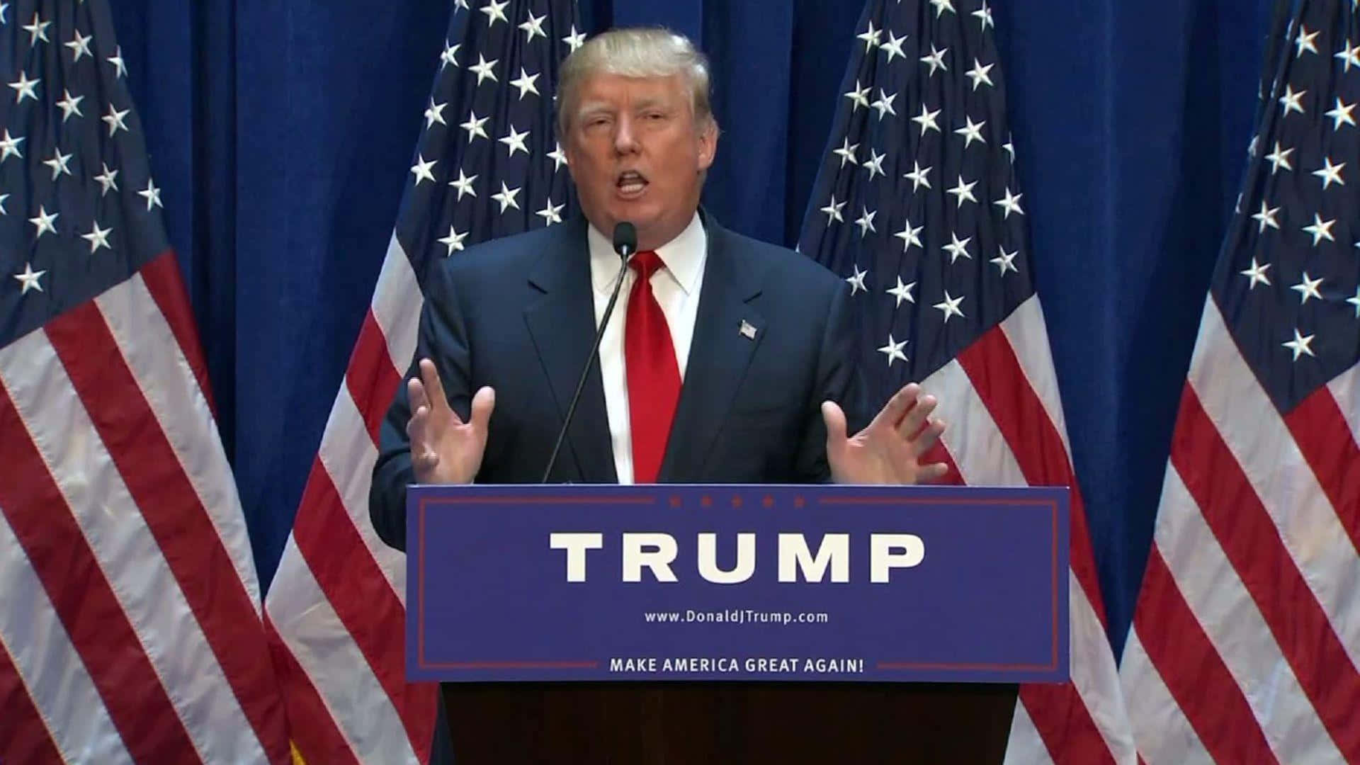 川普 桌布 壁紙 — 唐納·川普在講台上發言，講台上有「TRUMP」和「MAKE AMERICA GREAT AGAIN」字樣，兩側有美國國旗。