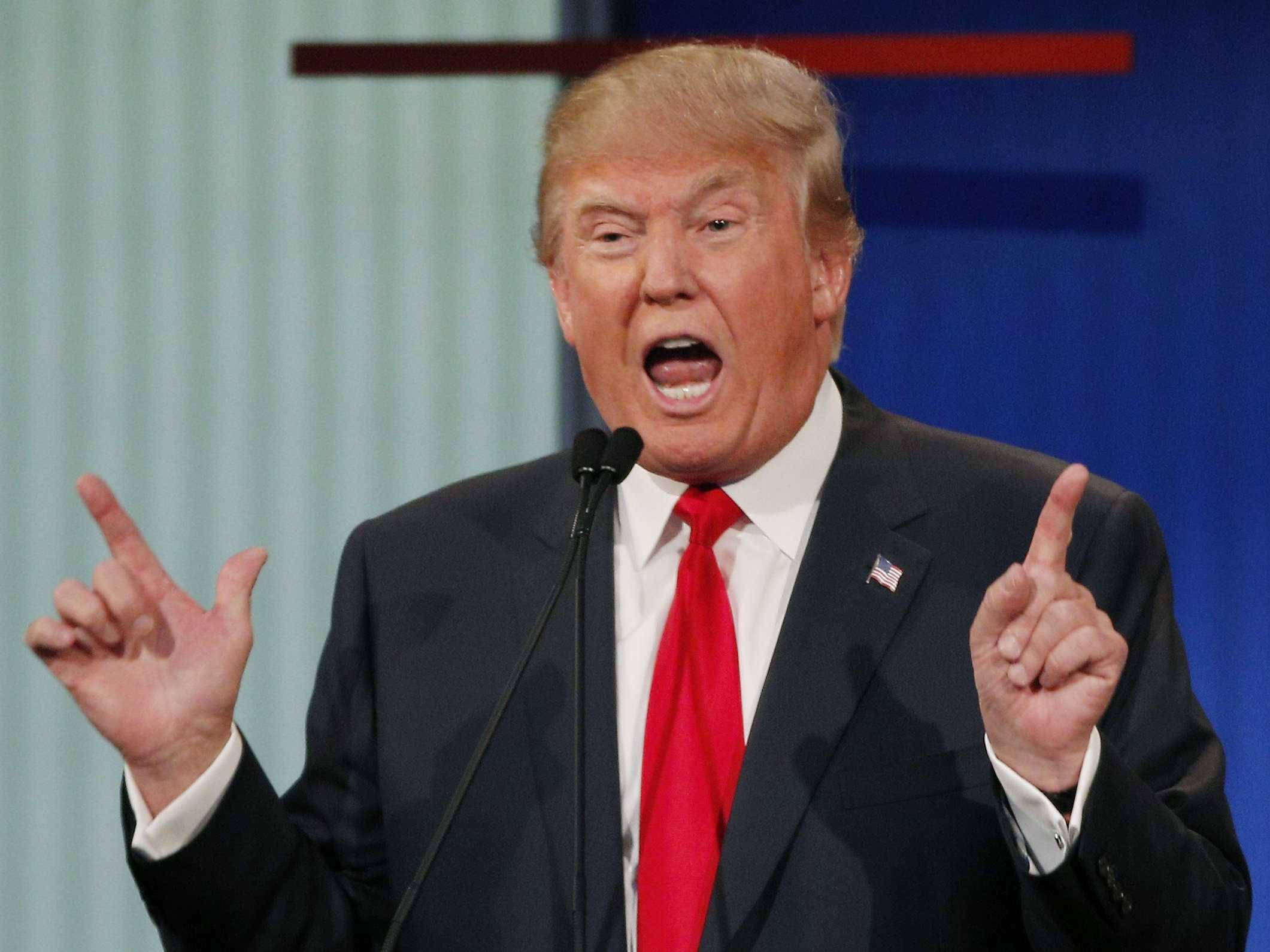 donald trump 桌布 壁紙 — 唐納·川普身穿深色西裝和紅色領帶，在政治活動中對著麥克風說話時，做出強調的手勢。