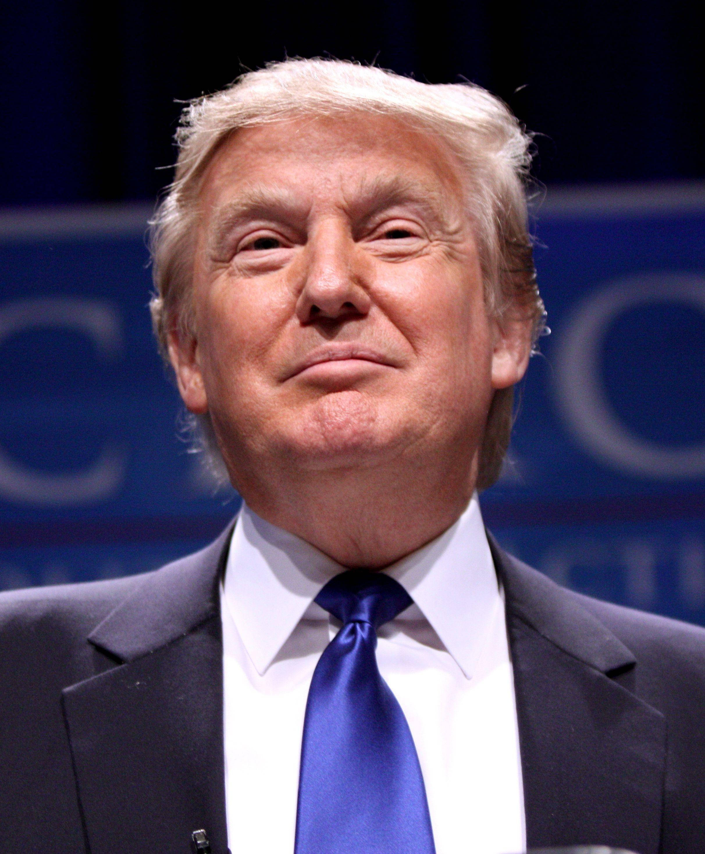 donald trump 桌布 壁紙 — 唐納德·特朗普身穿深色西裝和藍色領帶，背景模糊藍色的特寫肖像。
