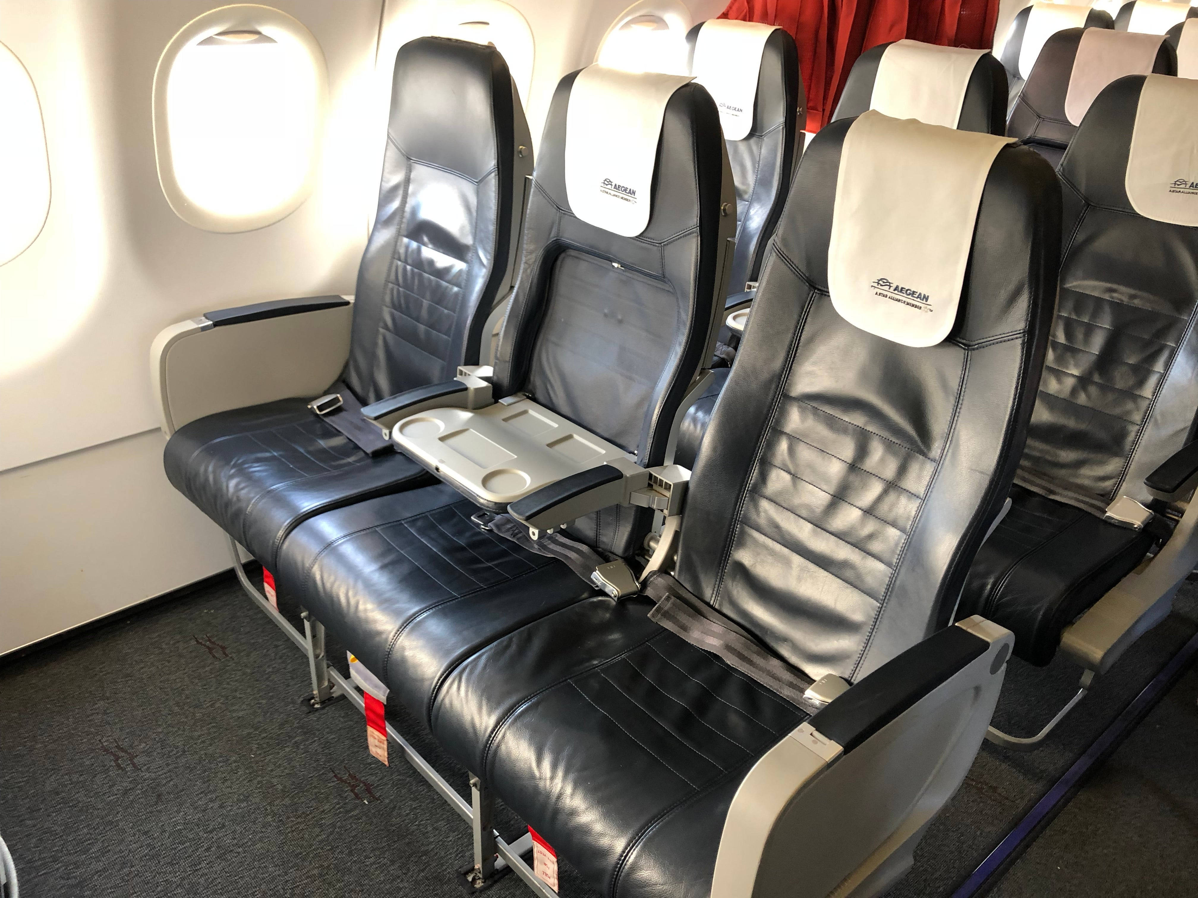 Plane 桌布 壁紙 — 商用飛機客艙內，一排排黑色皮革飛機座椅，附有托盤桌和窗景。