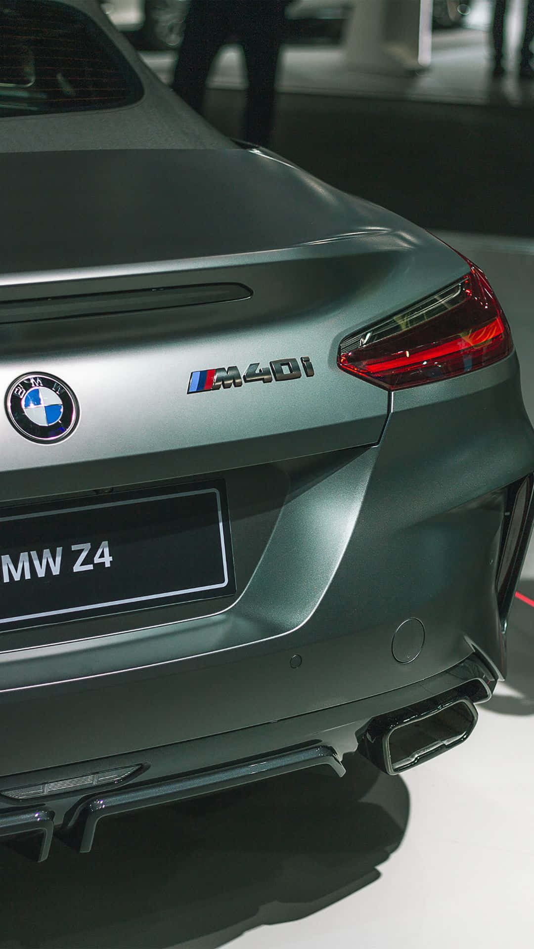 Android Bmw 桌布 壁紙 — 啞光灰色BMW Z4 M40i跑車尾部特寫，在明亮的展廳燈光下展示時尚尾燈和雙排氣管。