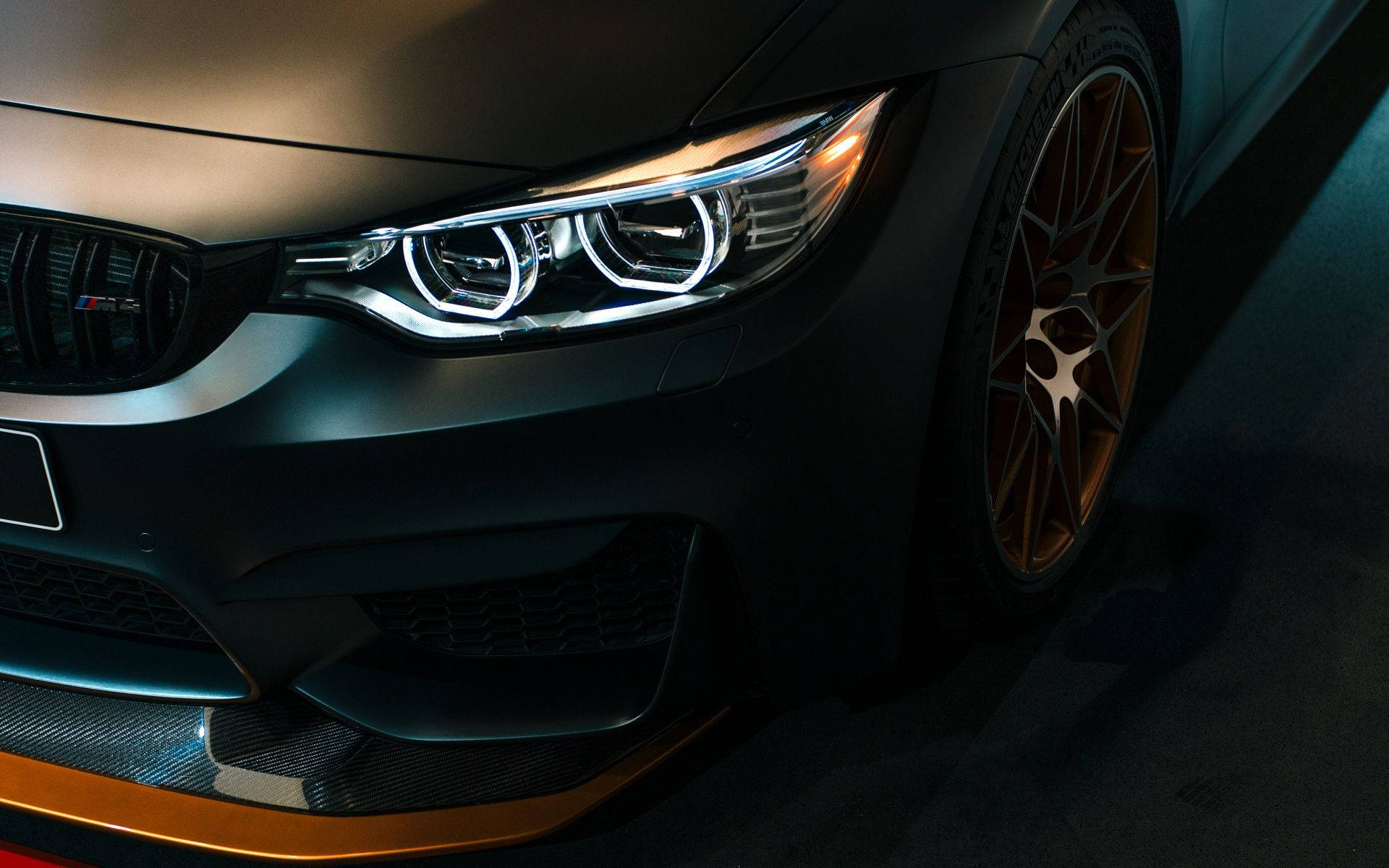 BMW 動圖 桌布 壁紙 — 啞光黑色BMW M4的特寫，帶有發光頭燈和金色輪圈，在戲劇性的工作室燈光下。