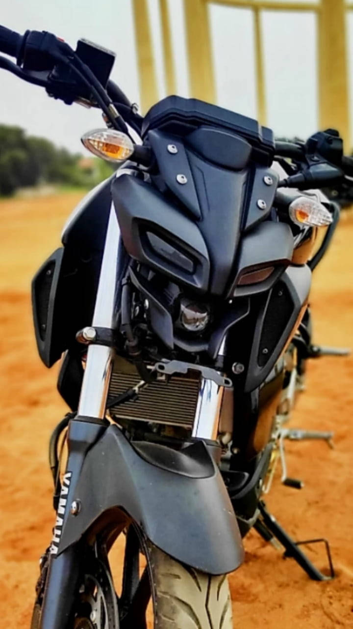 機車 桌布 壁紙 — 啞光黑色Yamaha摩托車近距離特寫，停在微紅泥土上，背景有模糊的黃色結構。