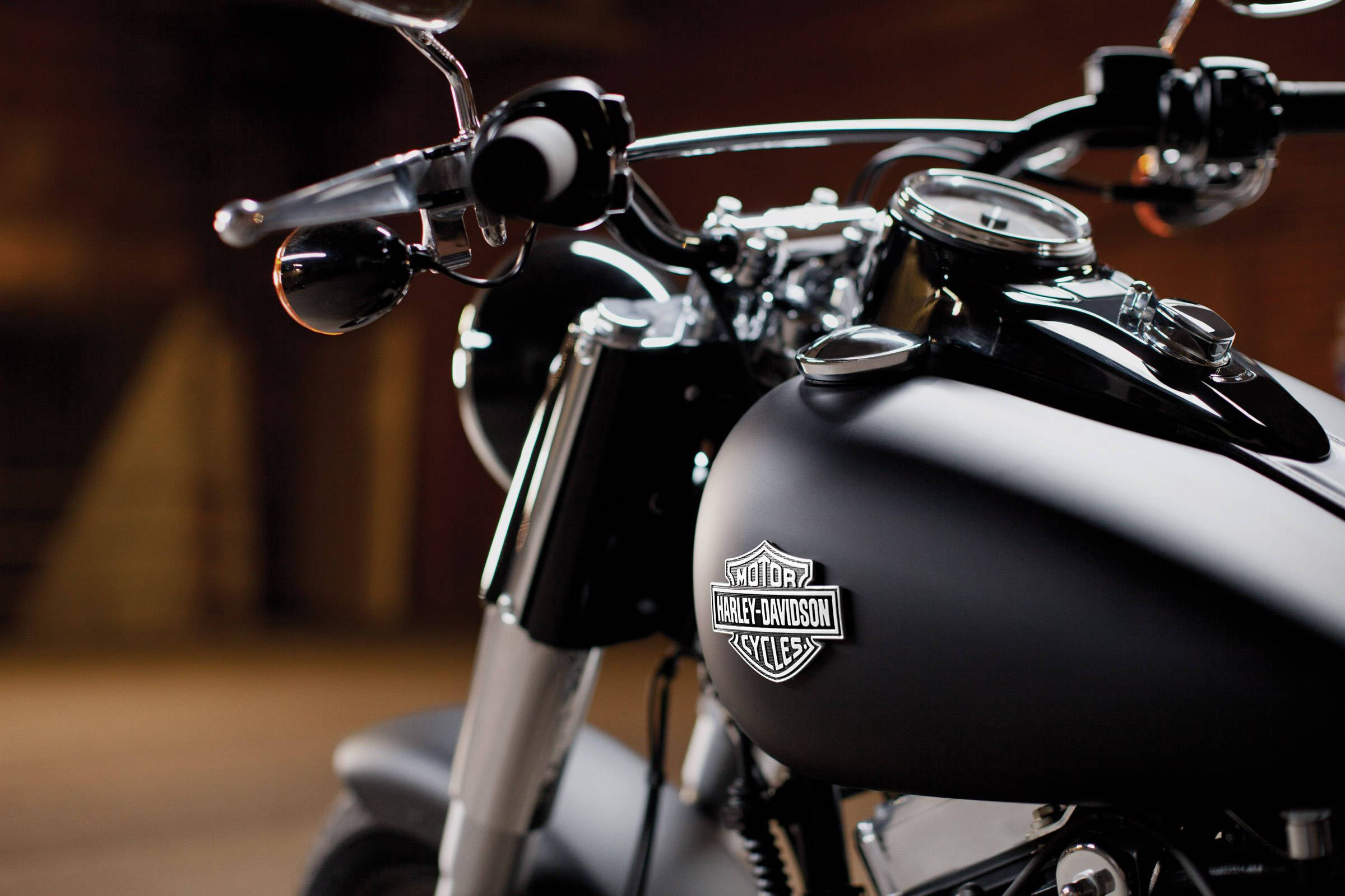 Harley 桌布 壁紙 — 啞光黑色哈雷戴維森摩托車的油箱和把手特寫，帶有鍍鉻裝飾，在昏暗的車庫中。