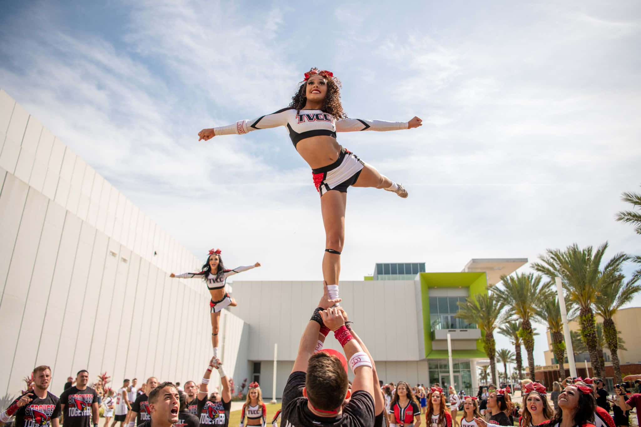 Cheer 桌布 壁紙 — 啦啦隊隊員身穿黑白制服，在棕櫚樹和明亮藍天下進行動態特技表演。