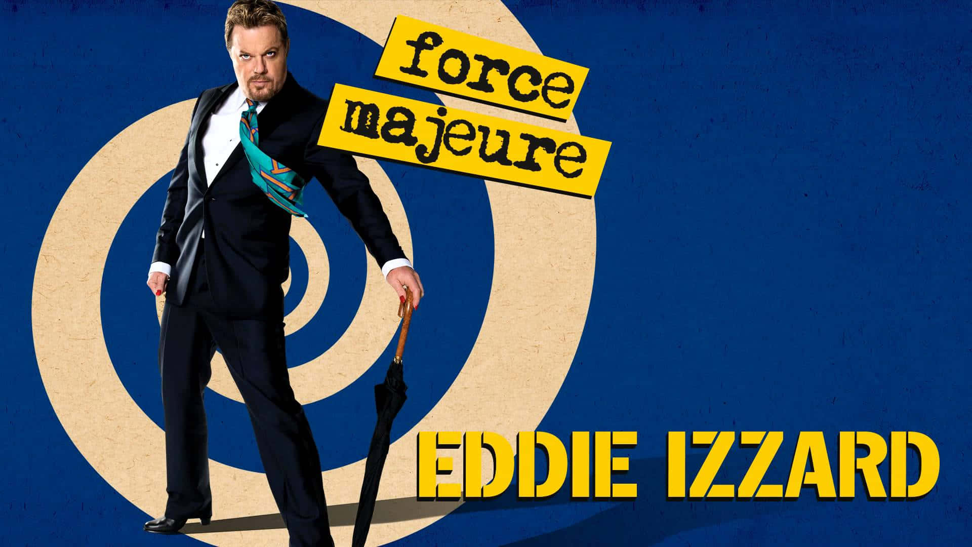 Eddie Izzard 桌布 壁紙 — 喜劇演員艾迪·伊扎德身穿俐落西裝，自信地站在大膽的藍色背景前，背景有同心圓和黃色文字「force majeure」。