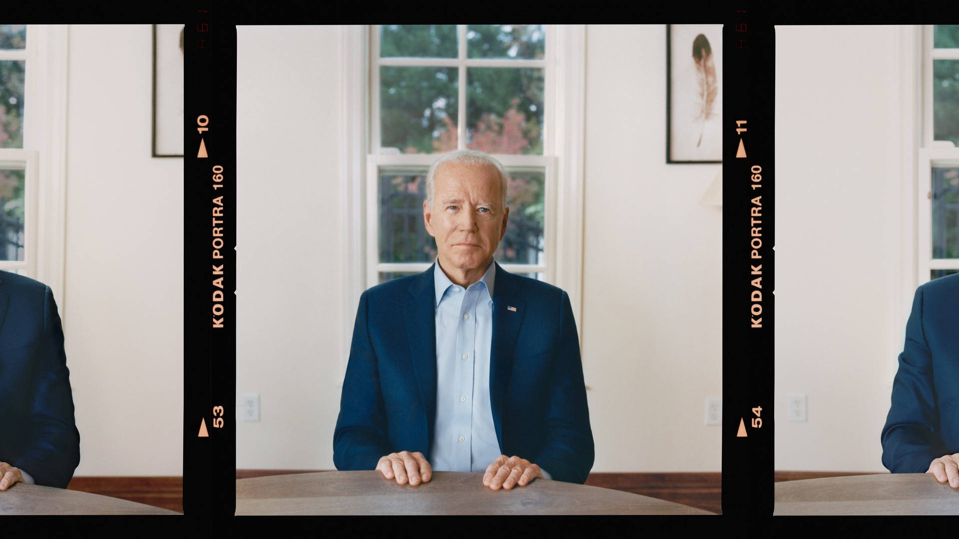 Biden 桌布 壁紙 — 喬·拜登的正式肖像，坐在木桌旁，房間明亮，大窗戶顯示外面的綠意。