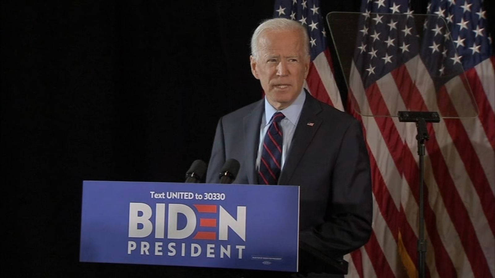 Biden 桌布 壁紙 — 喬·拜登站在藍色「Biden President」講台上，背後有美國國旗，正在進行競選演講。